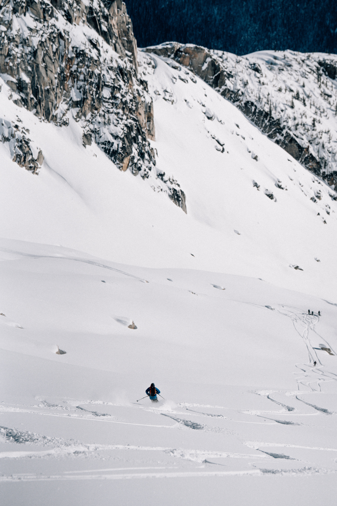 A lone skier below granite walls, the rest of the group waiting above