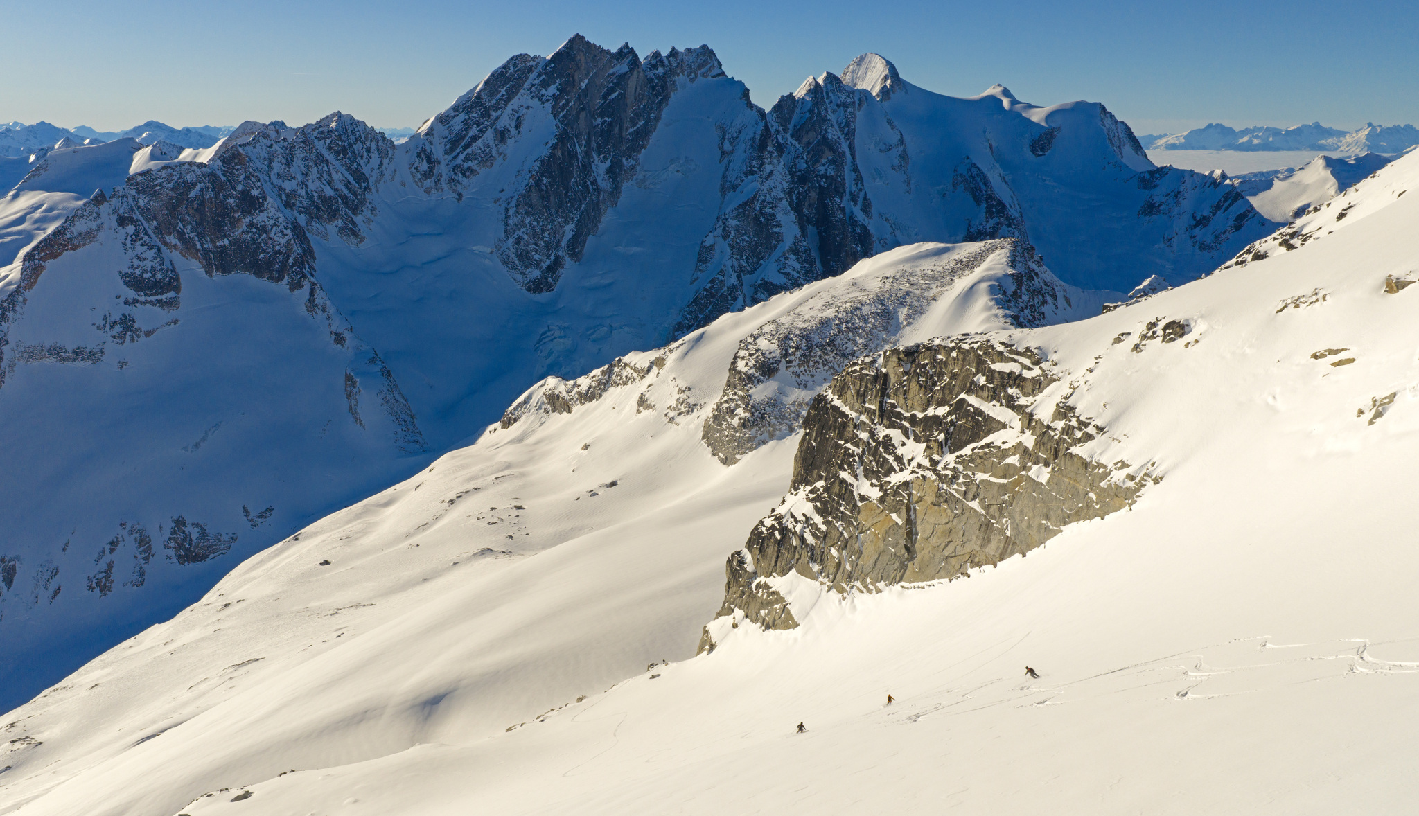 Ski tourers crossing a sunlit slope beneath jagged peaks