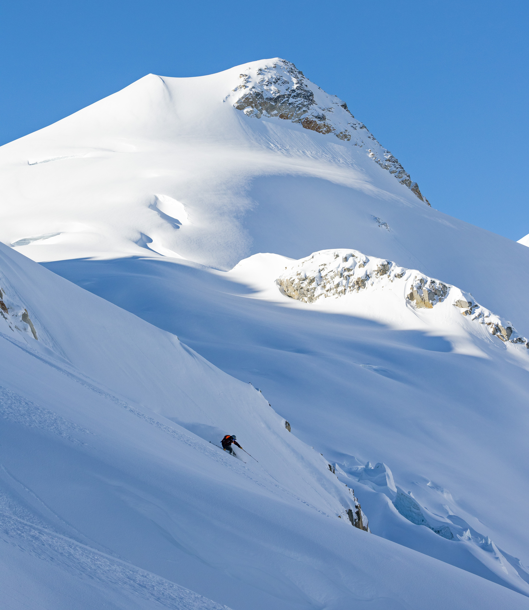 A lone skier far below a snow-plastered summit