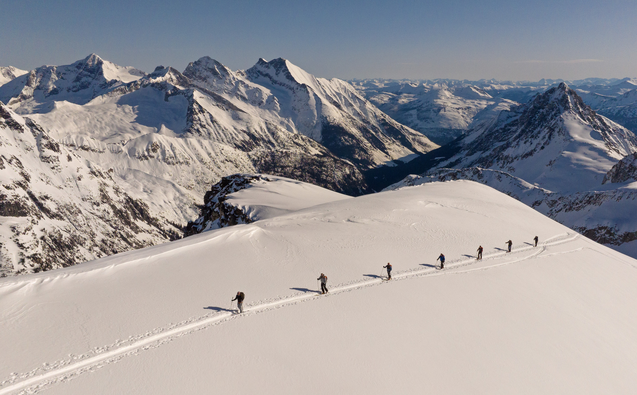 A group crossing a broad snow shoulder toward the peaks