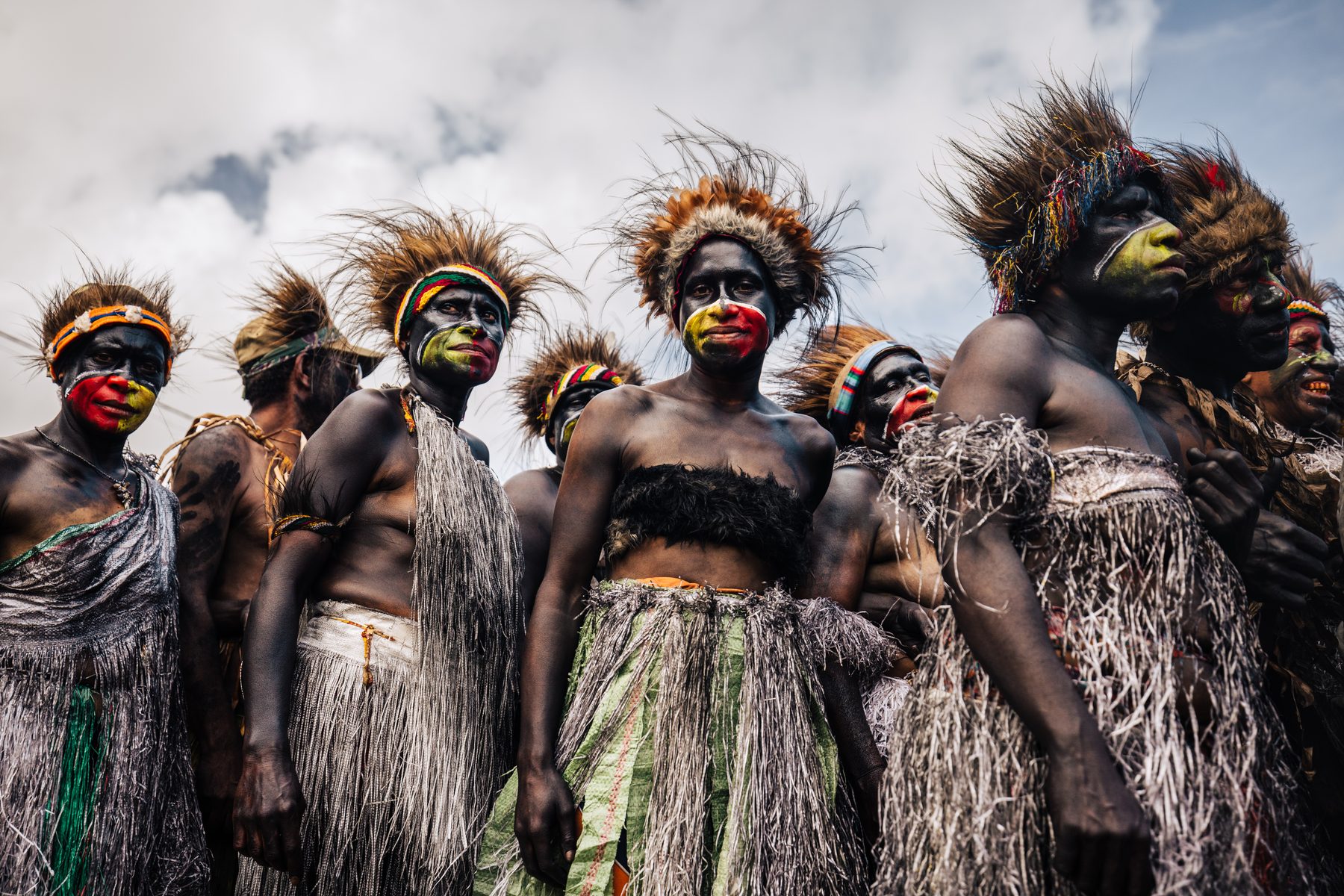 A sing-sing group in grass skirts and feathered headdresses against the sky at Mount Hagen