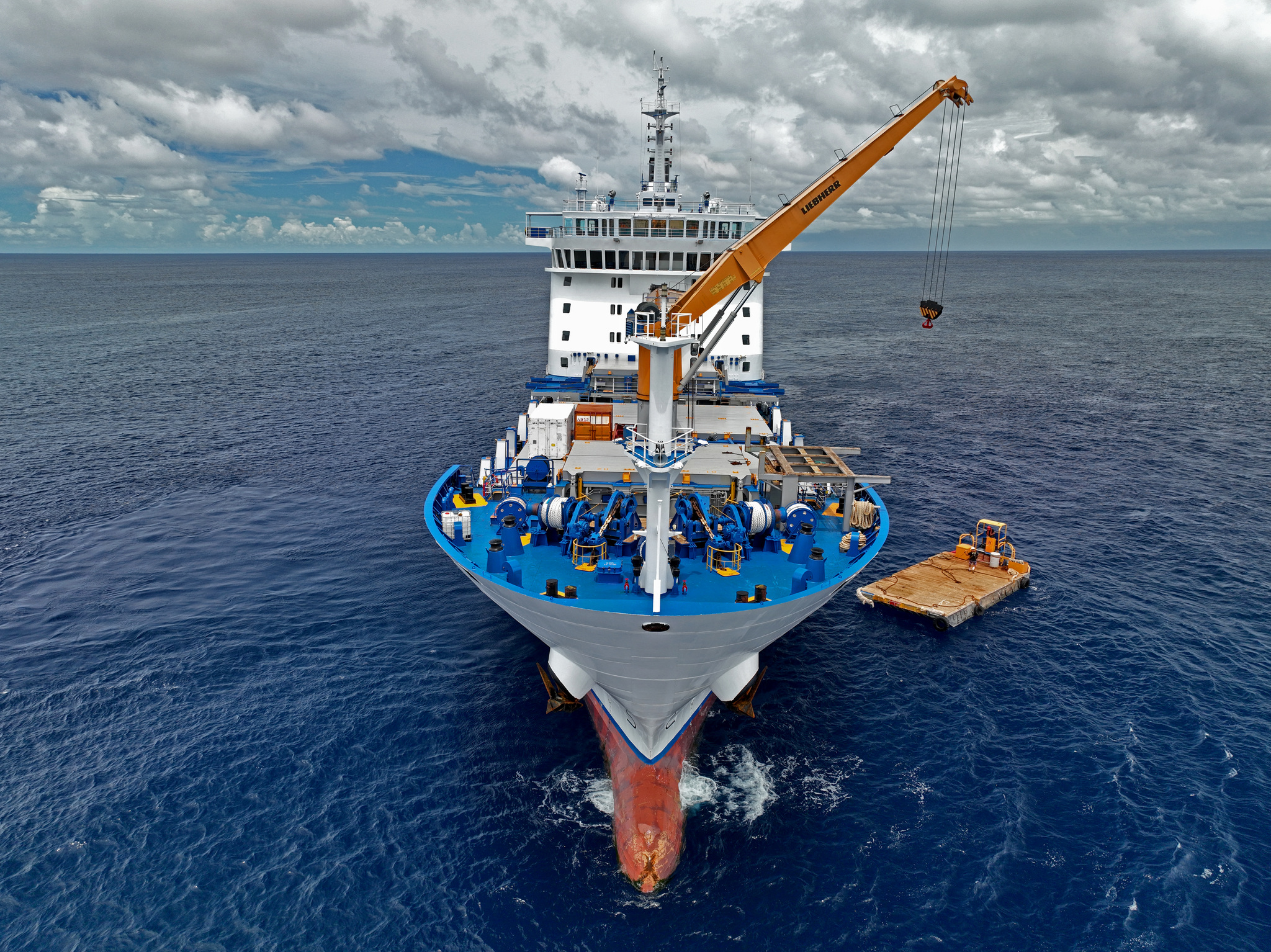 The bow and forward crane of Aranui 5, with a cargo barge alongside, from above