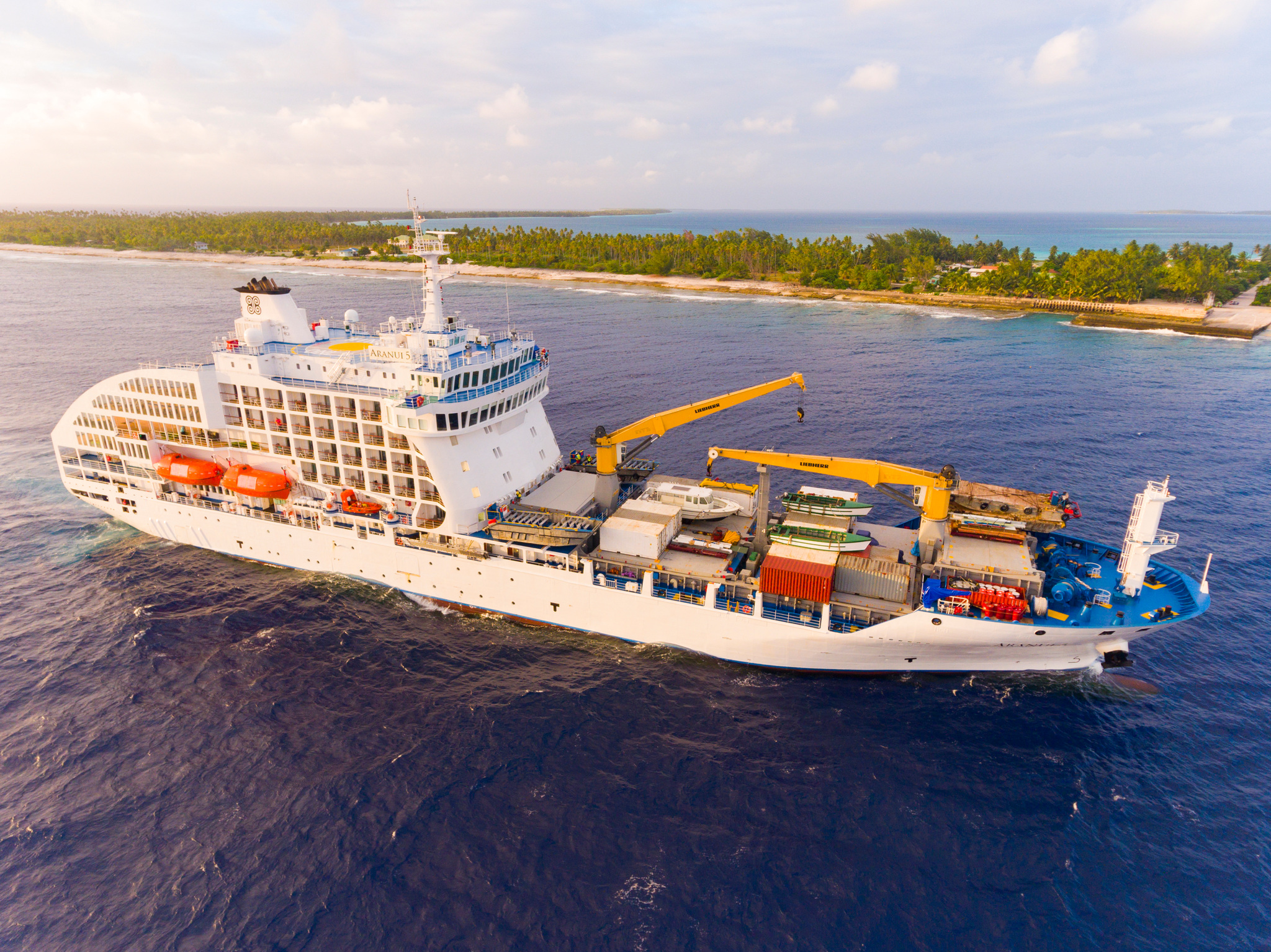 Aranui 5 off an atoll with her two yellow cranes and containers forward