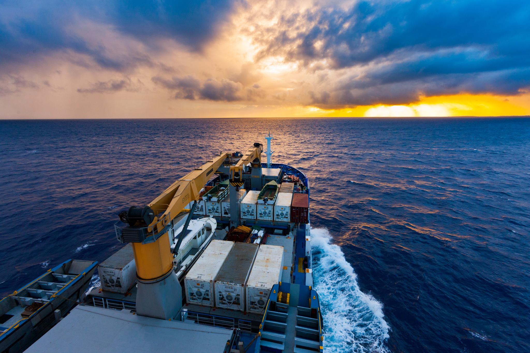Containers and a crane on the forward deck as the ship sails toward the sunset