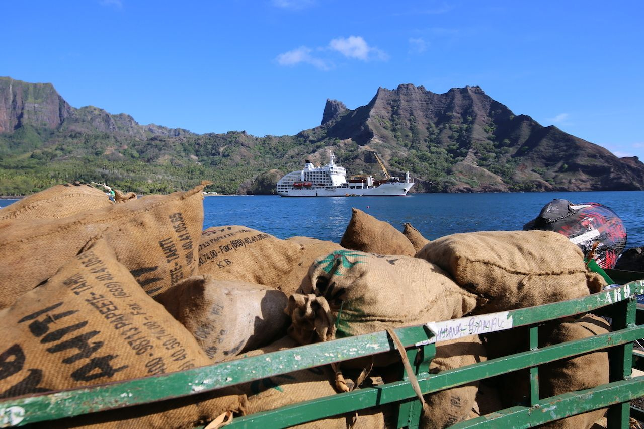 Sacks of copra on a truck at the quay, Aranui 5 in the bay below the mountains