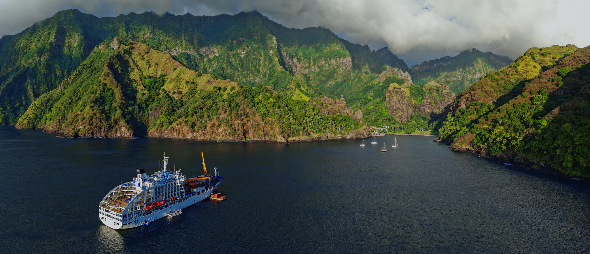Aranui 5 at anchor in Hanavave Bay on Fatu Hiva, below green ridges, yachts moored off the village