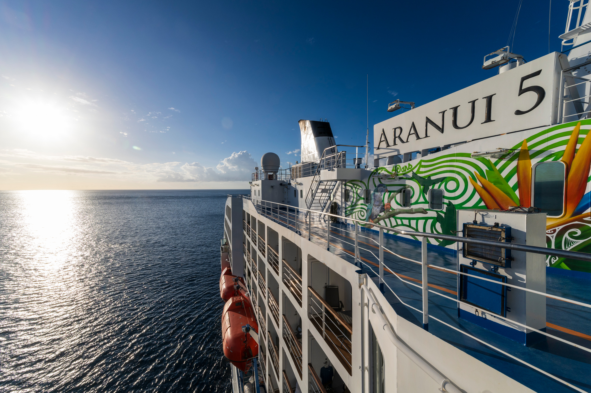 The ship's name and a painted mural on her side, the low sun over the sea beyond