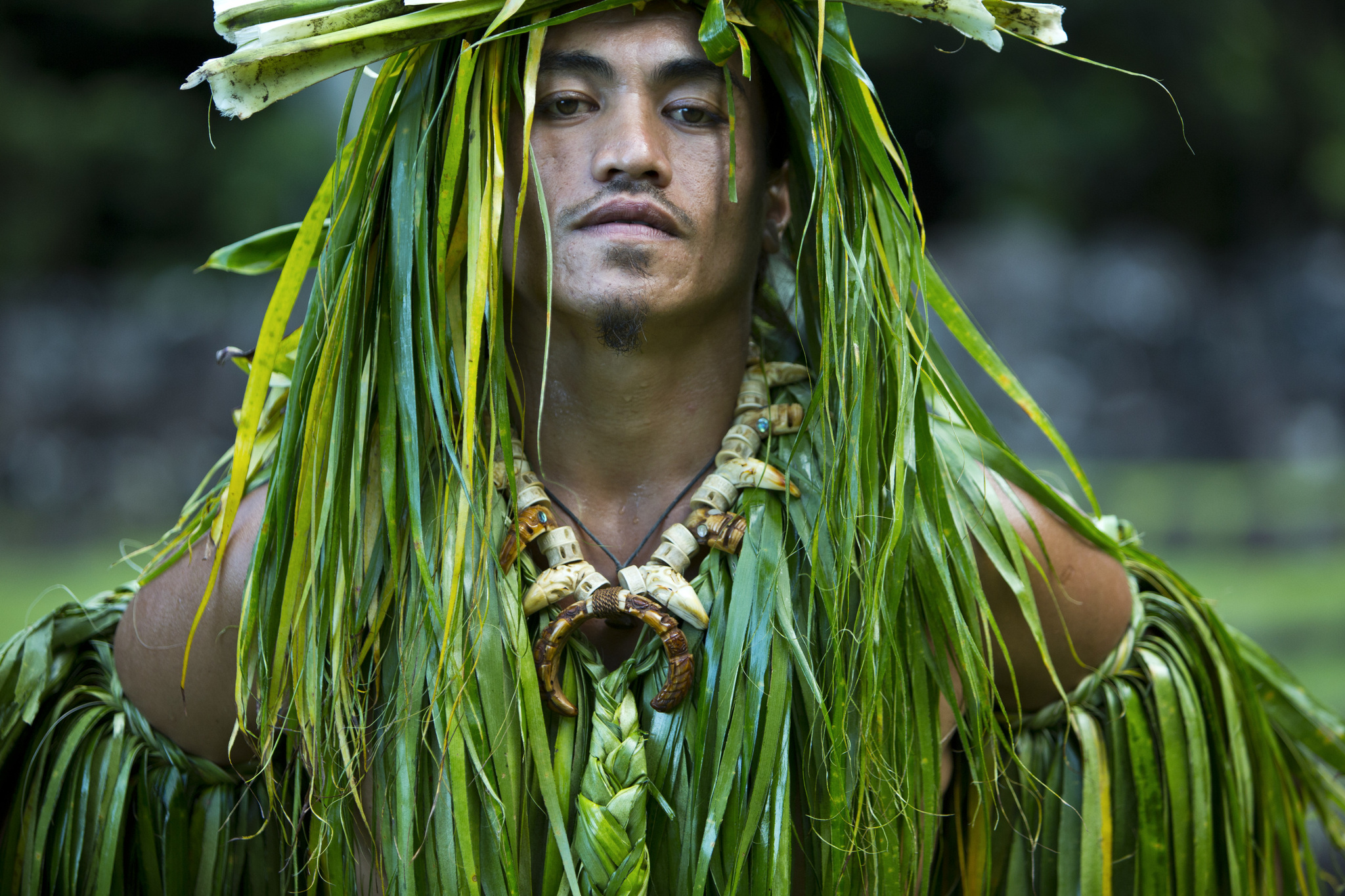A dancer in a costume of long green leaves and a bone necklace