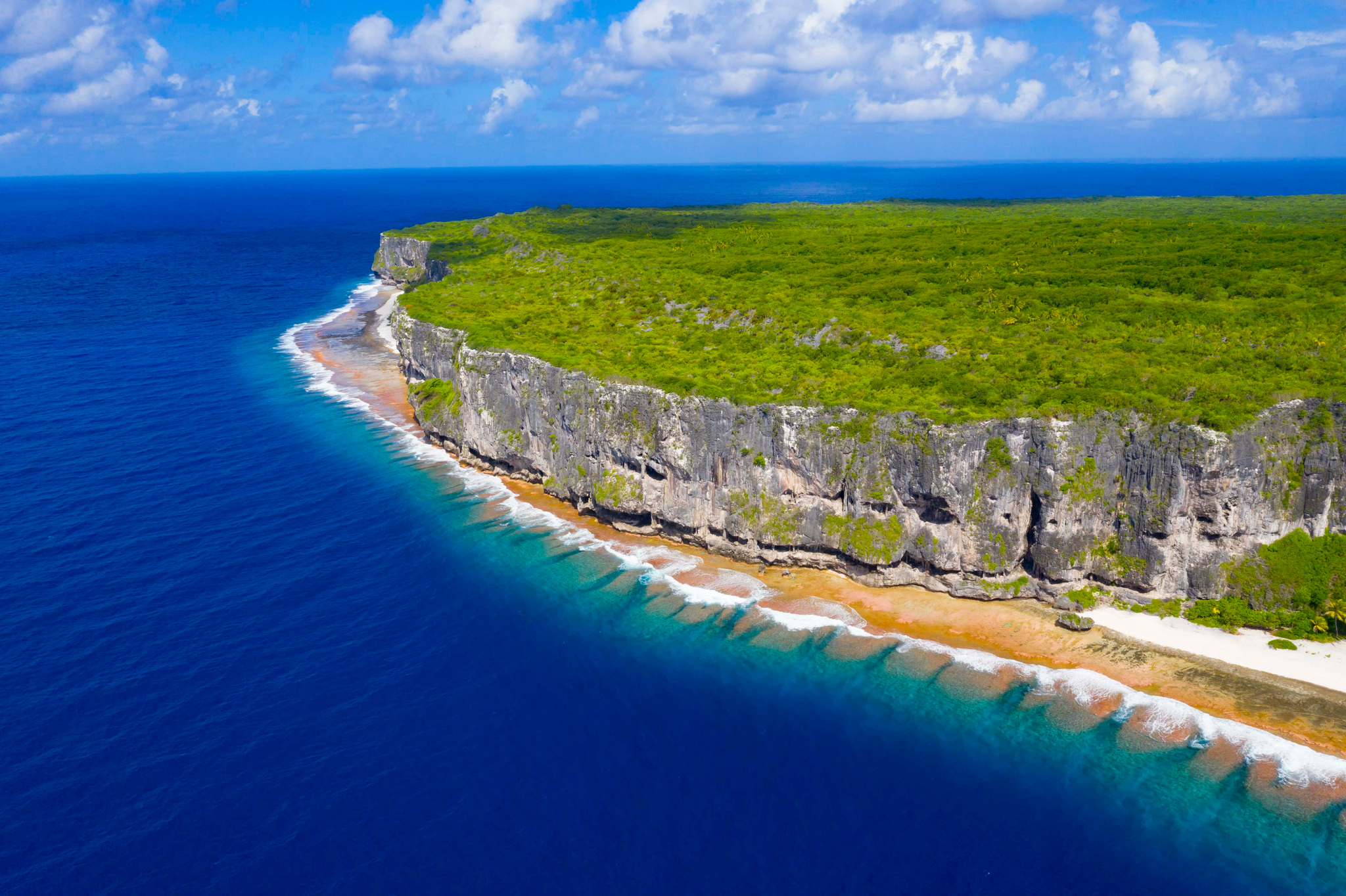 The raised coral cliffs of Makatea above a narrow beach and reef, from the air