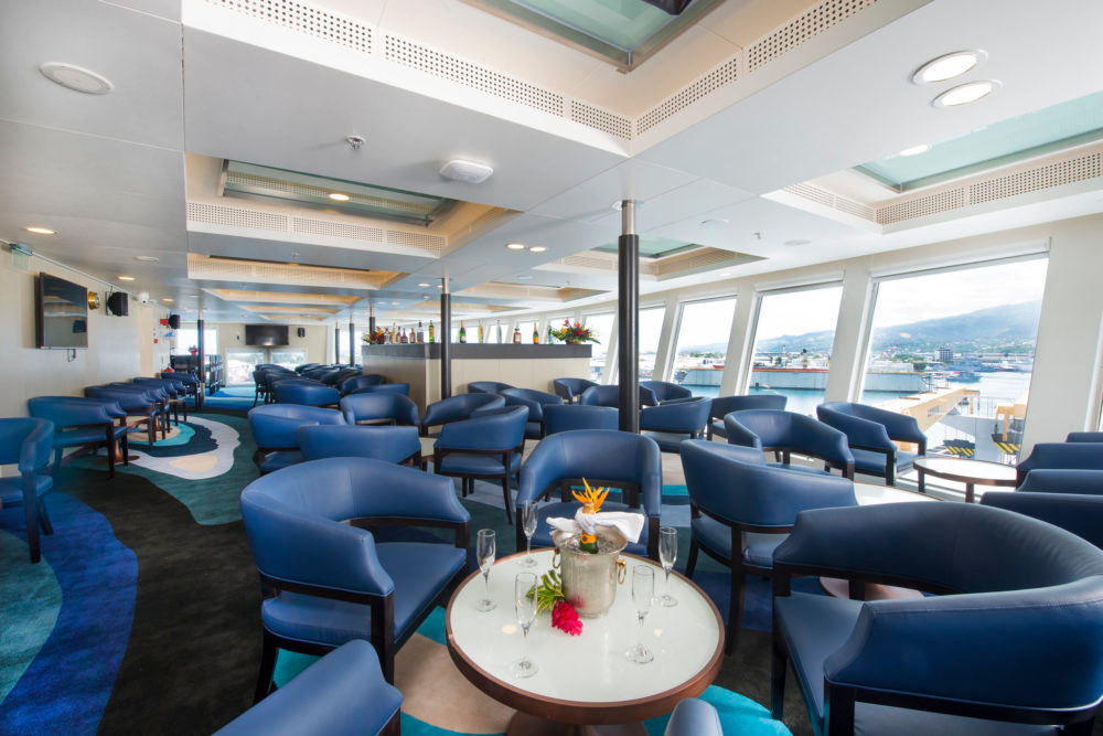 A lounge with blue armchairs, a bar and wide windows onto the harbour