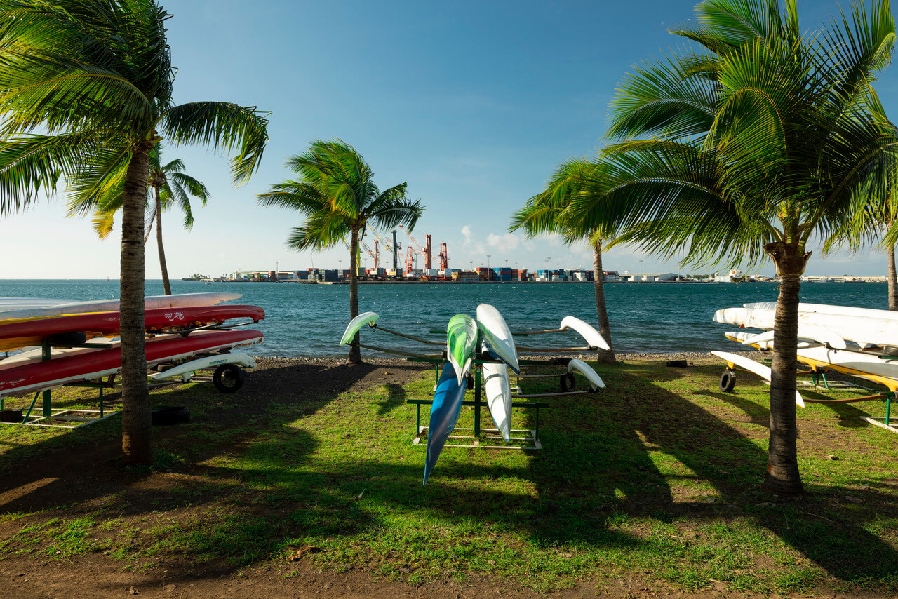 Outrigger canoes racked under palms on the Papeete waterfront, the port across the water