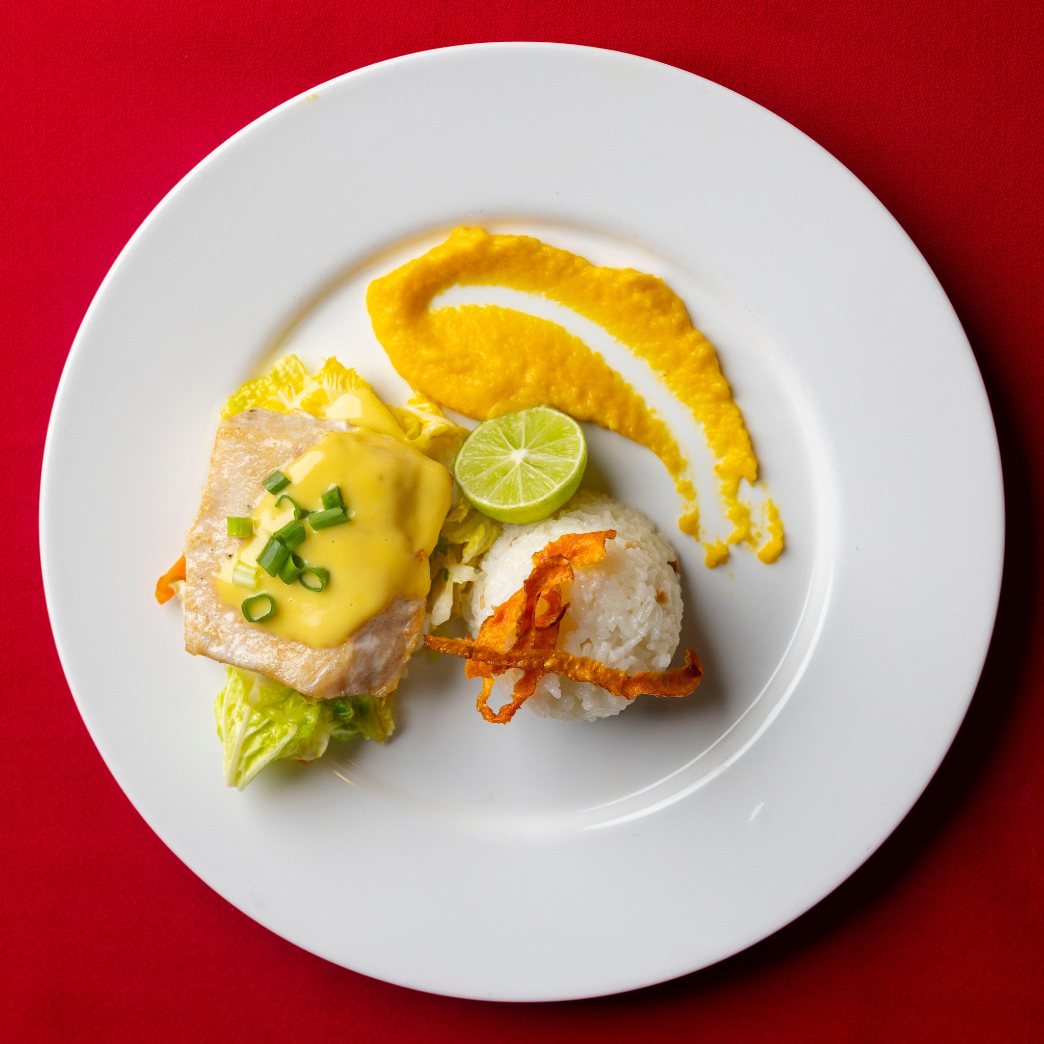 A fish fillet with a yellow sauce, lime and greens on a white plate