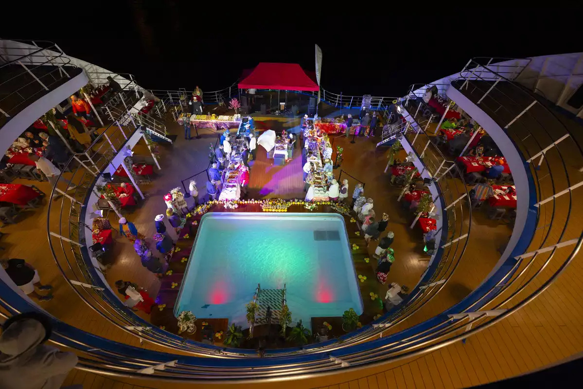 The pool deck at night, lit up and laid with a buffet, from above