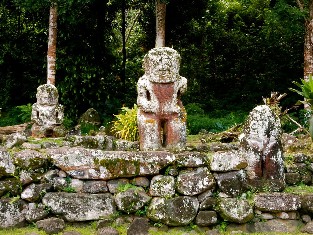 Stone tikis on a stone platform among palms at Puamau