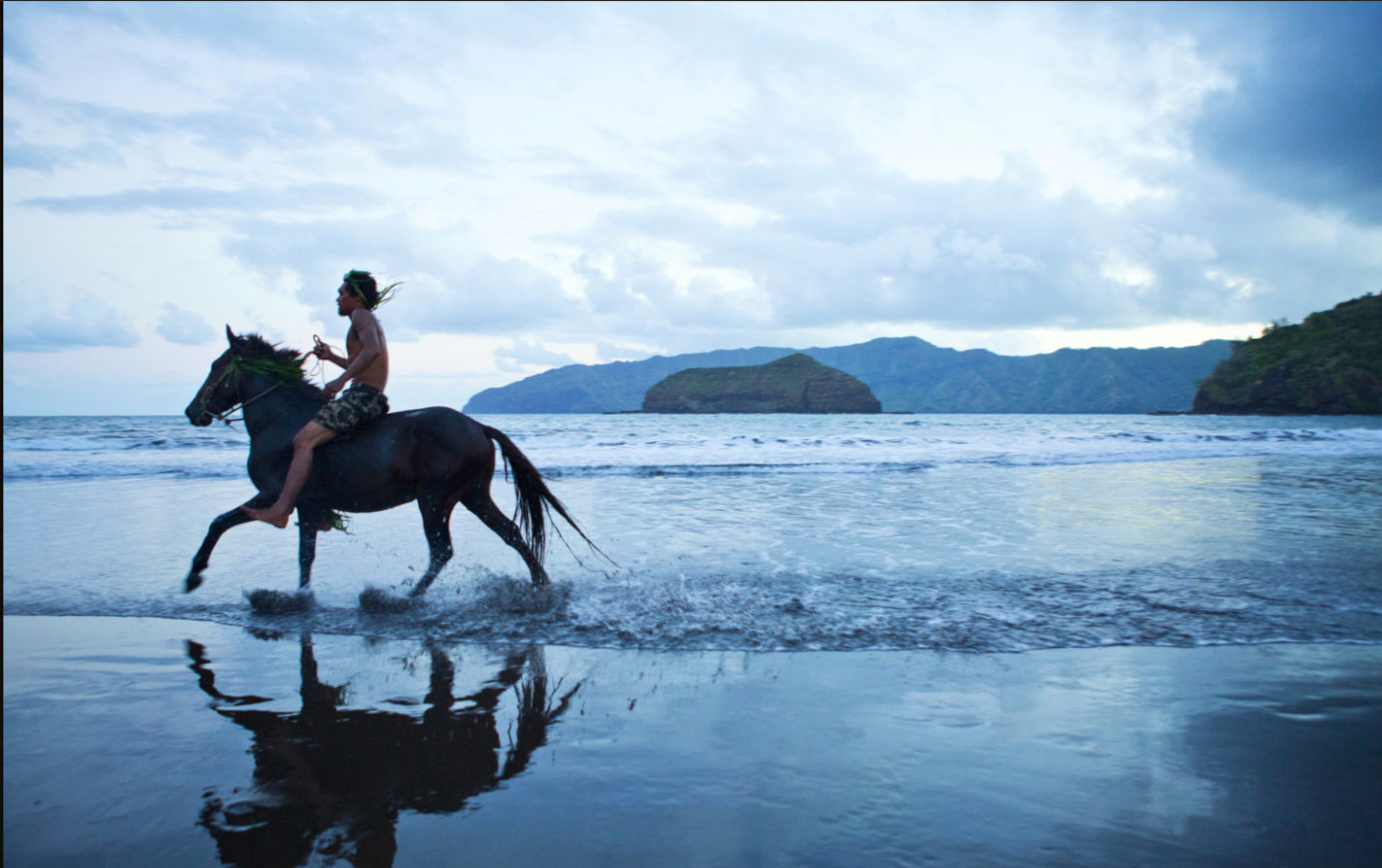 A rider galloping bareback through the shallows of a bay