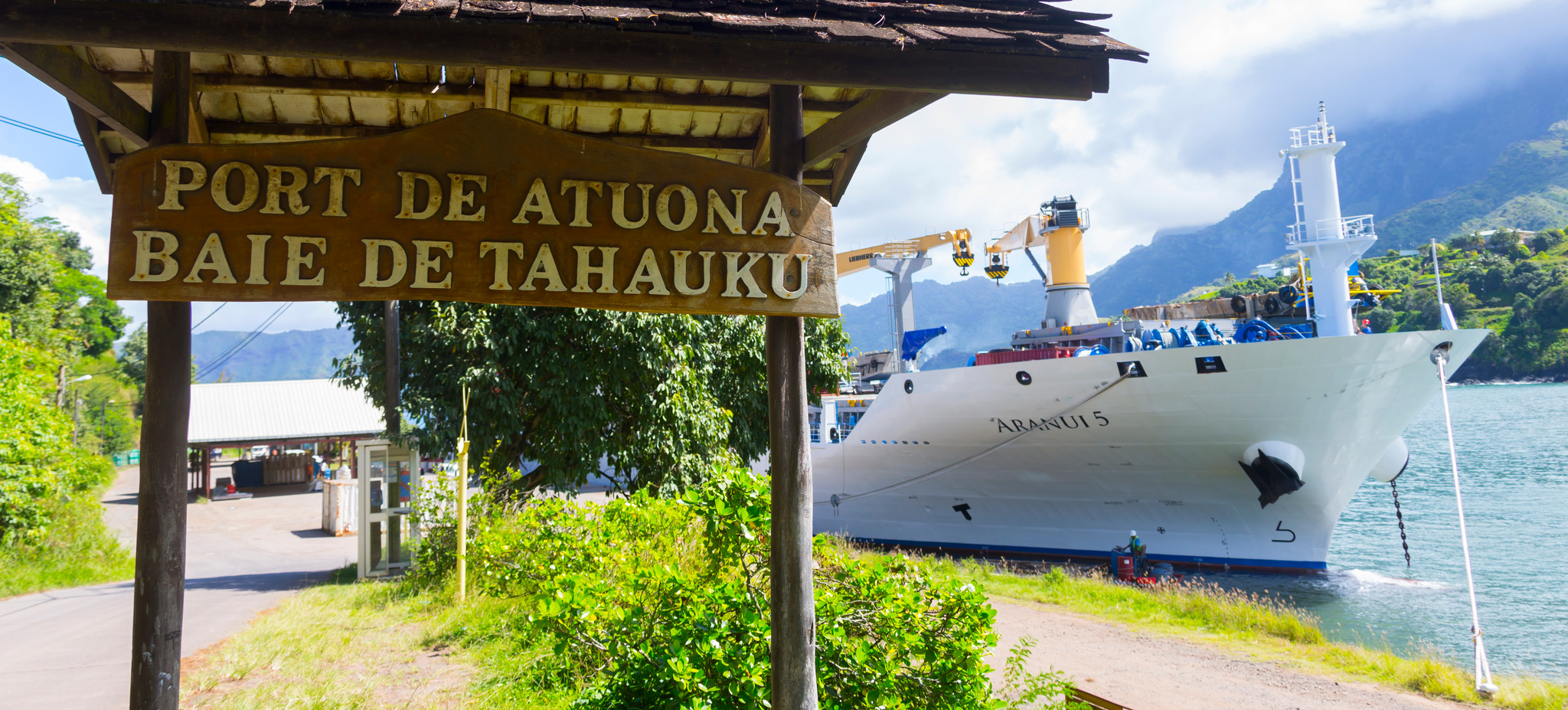 Aranui 5 at the quay in Tahauku Bay, beside the port's wooden sign for Atuona