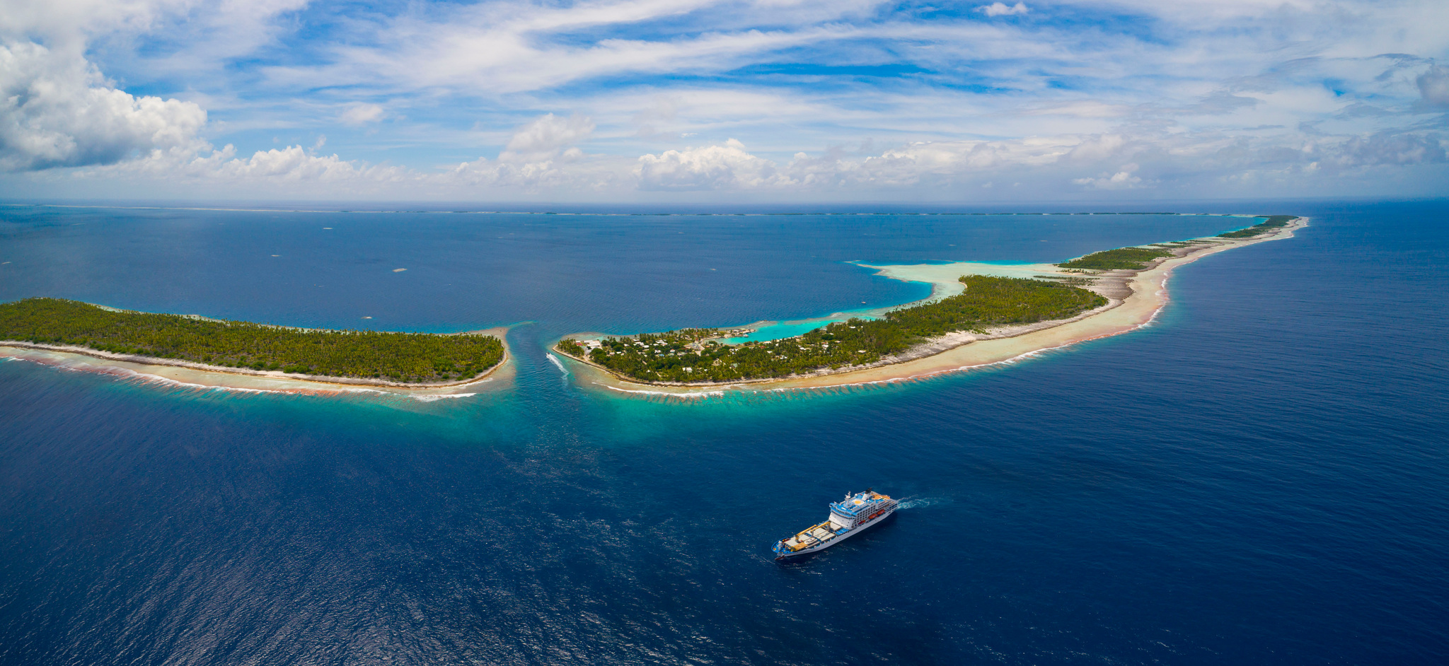 Aranui 5 approaching the pass between two islets of an atoll, from the air