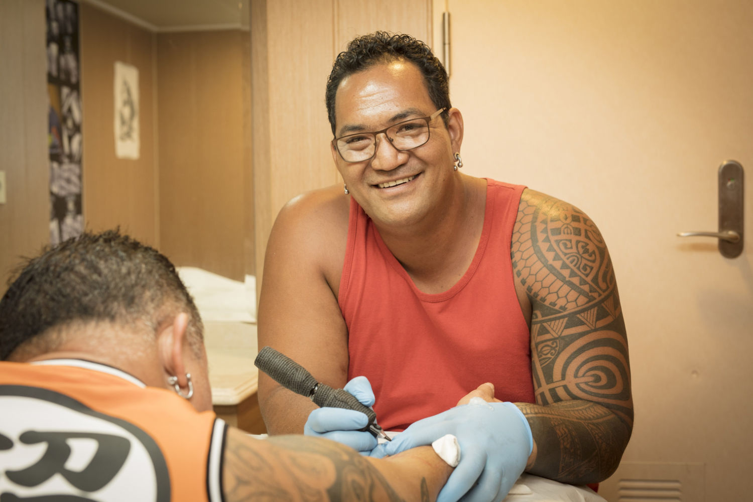 The tattoo artist aboard, smiling, at work in gloves on a client's arm