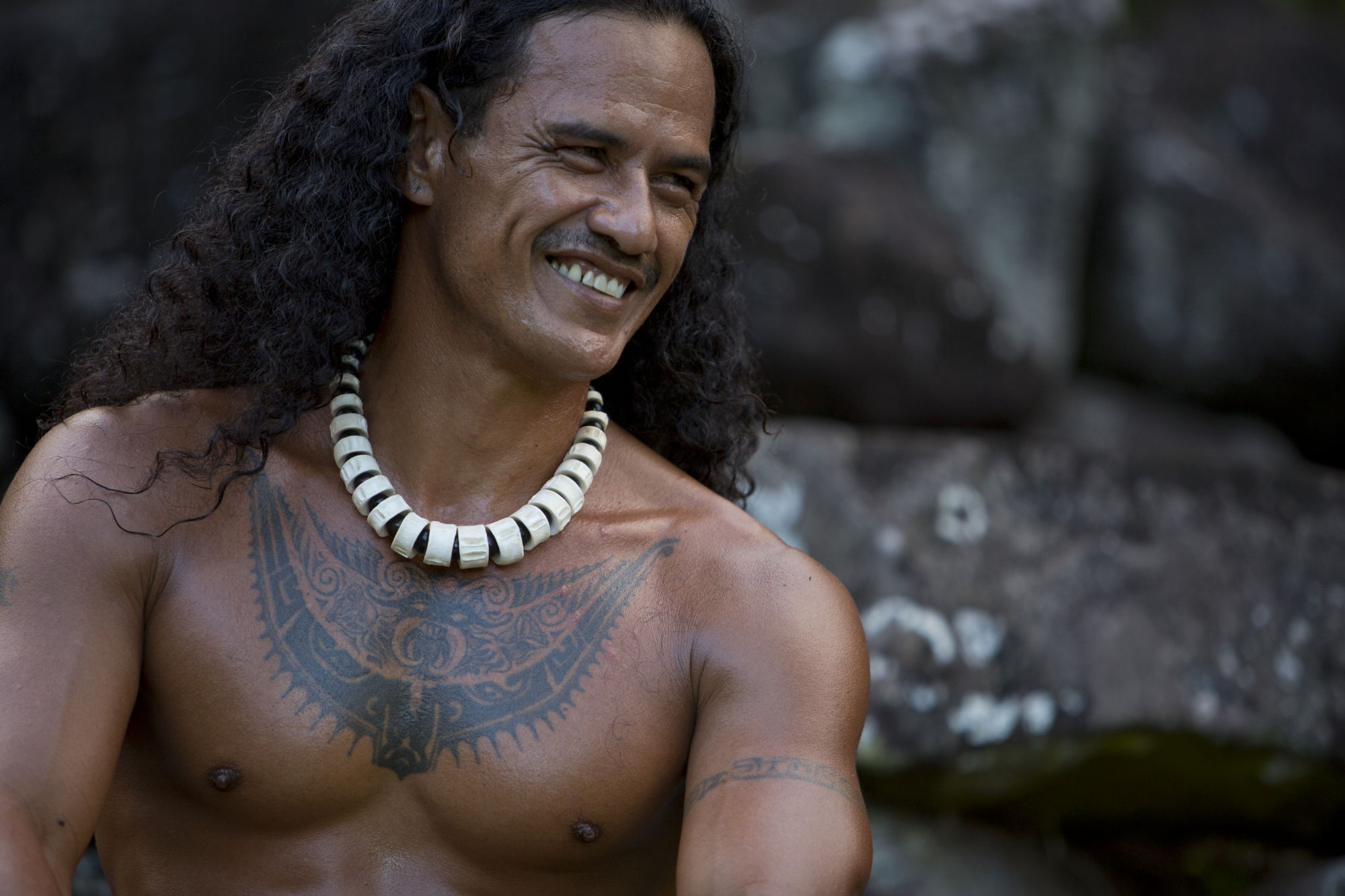 A smiling Marquesan man with a tattooed chest and a bone necklace