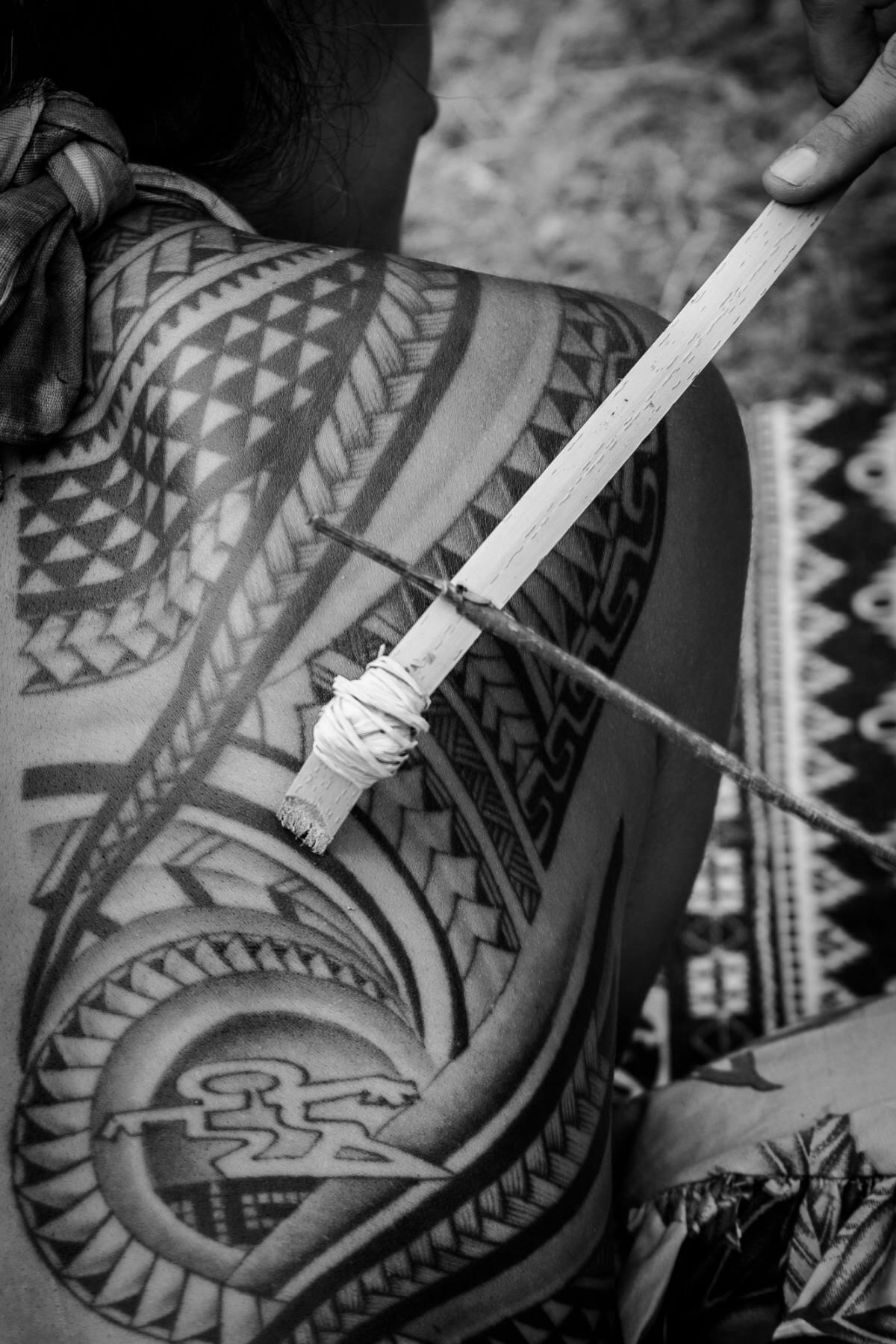 A traditional tattooing comb tapped against a tattooed back, in black and white