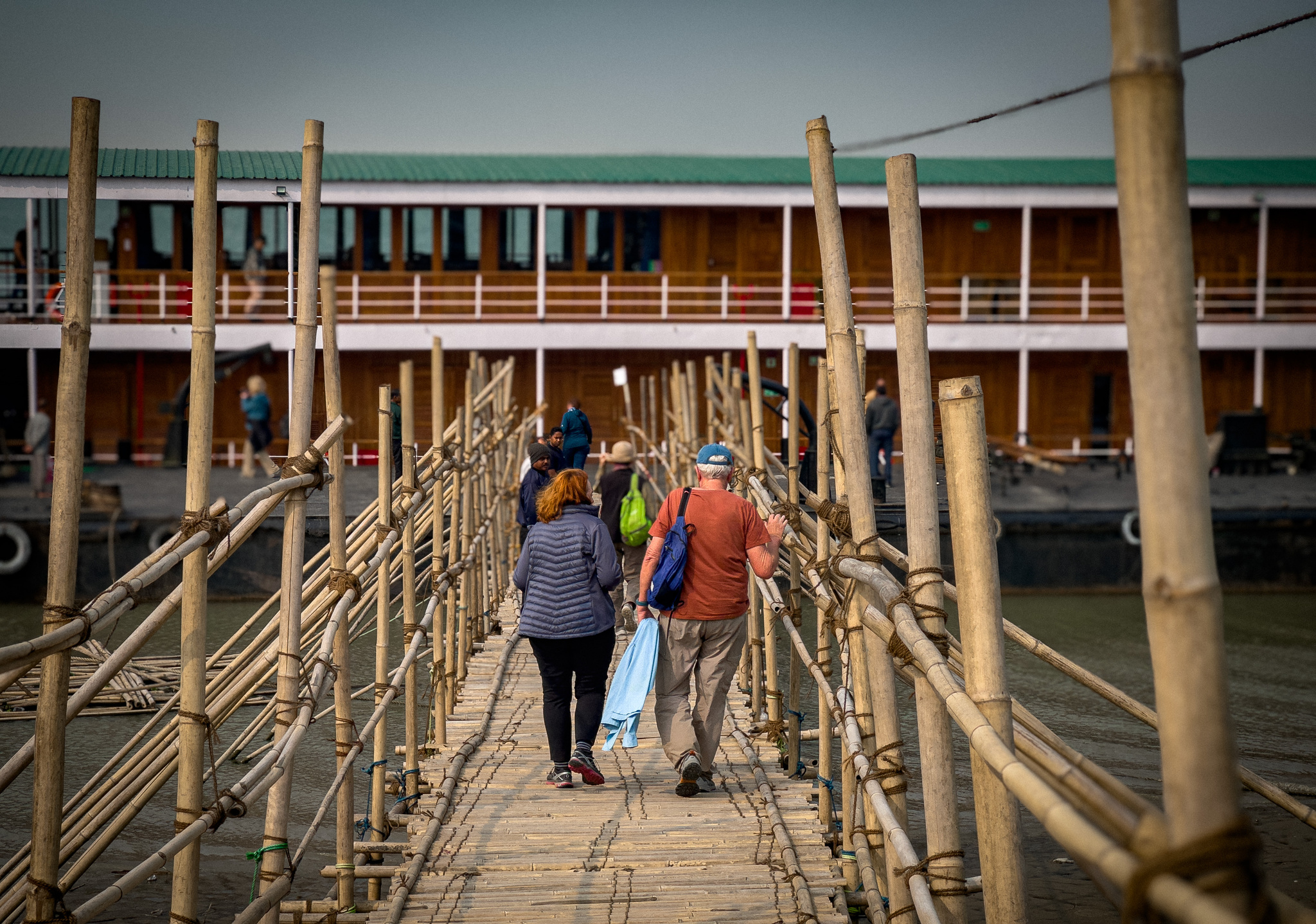 Guests crossing a long bamboo gangway to the ship