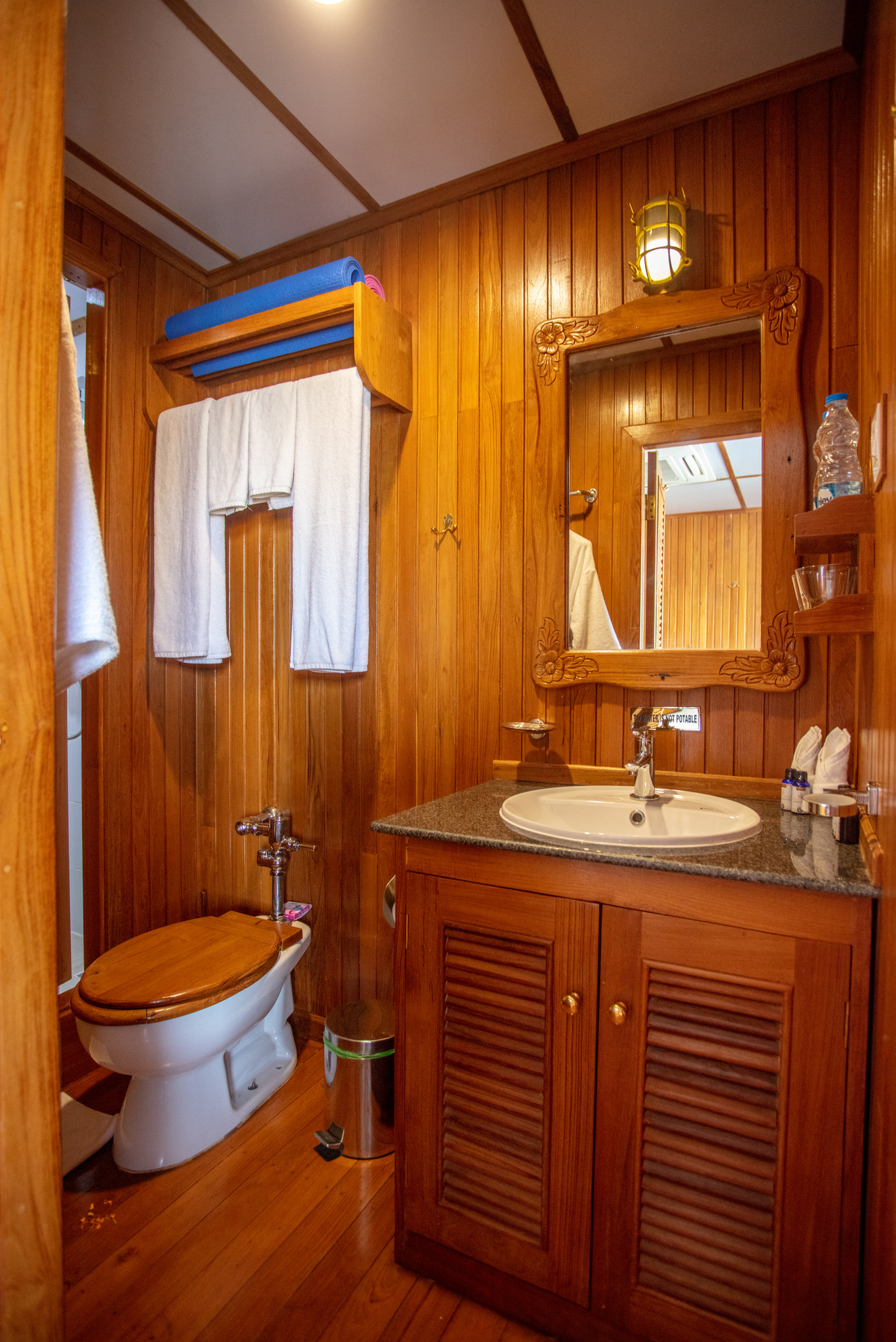 A cabin bathroom in teak, with a basin and a mirror