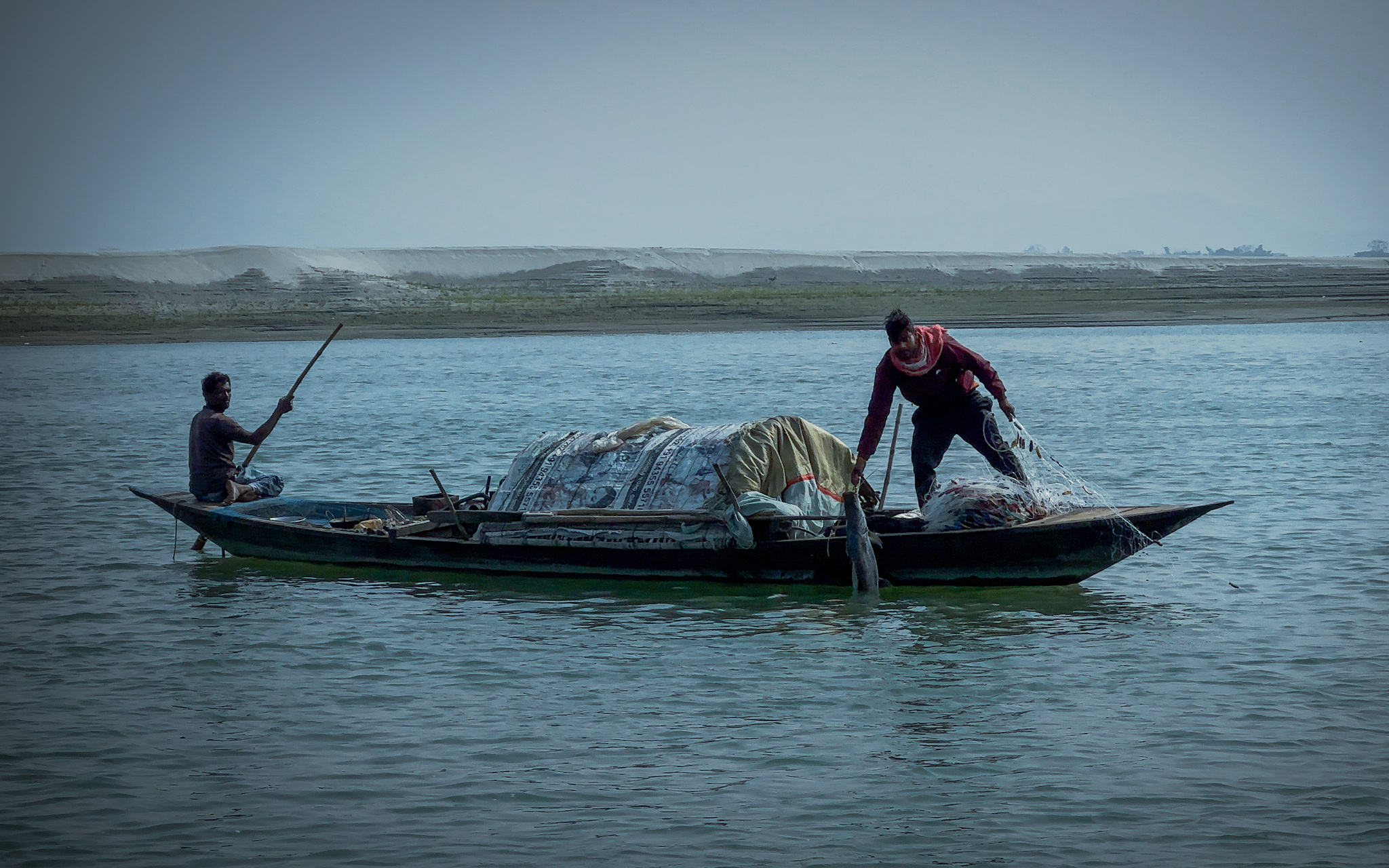 Two fishermen working a net from a wooden boat