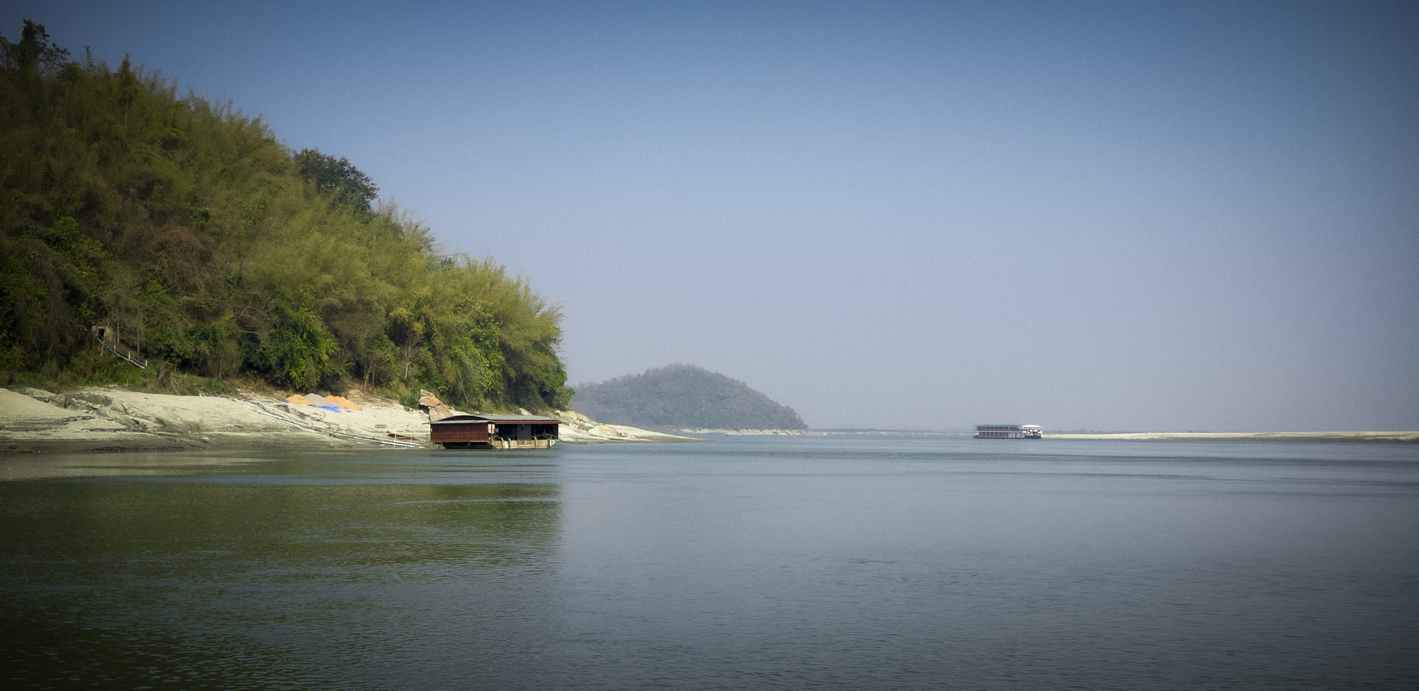 A forested hill above the river in the haze