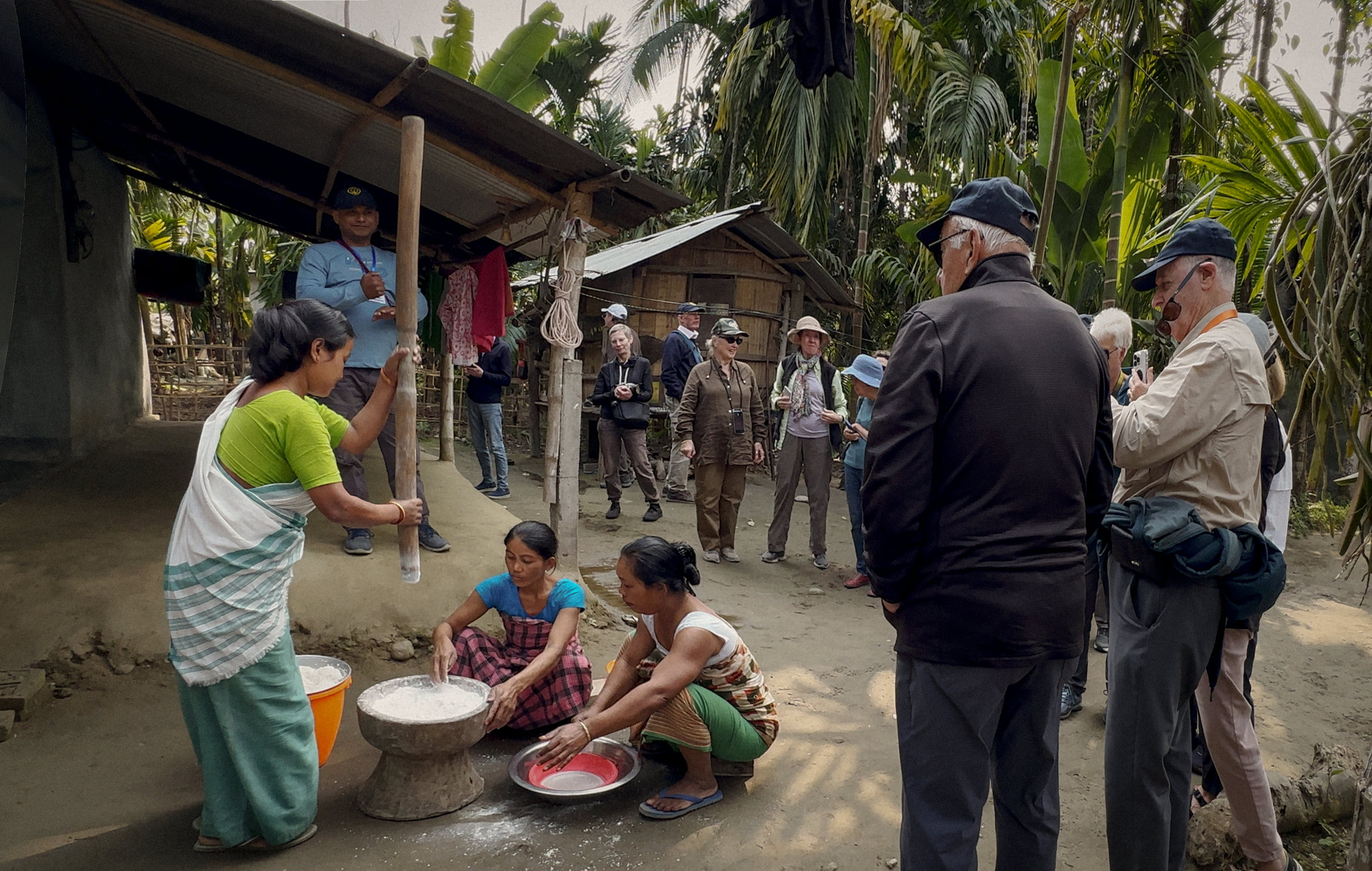 Village women pounding rice as guests look on