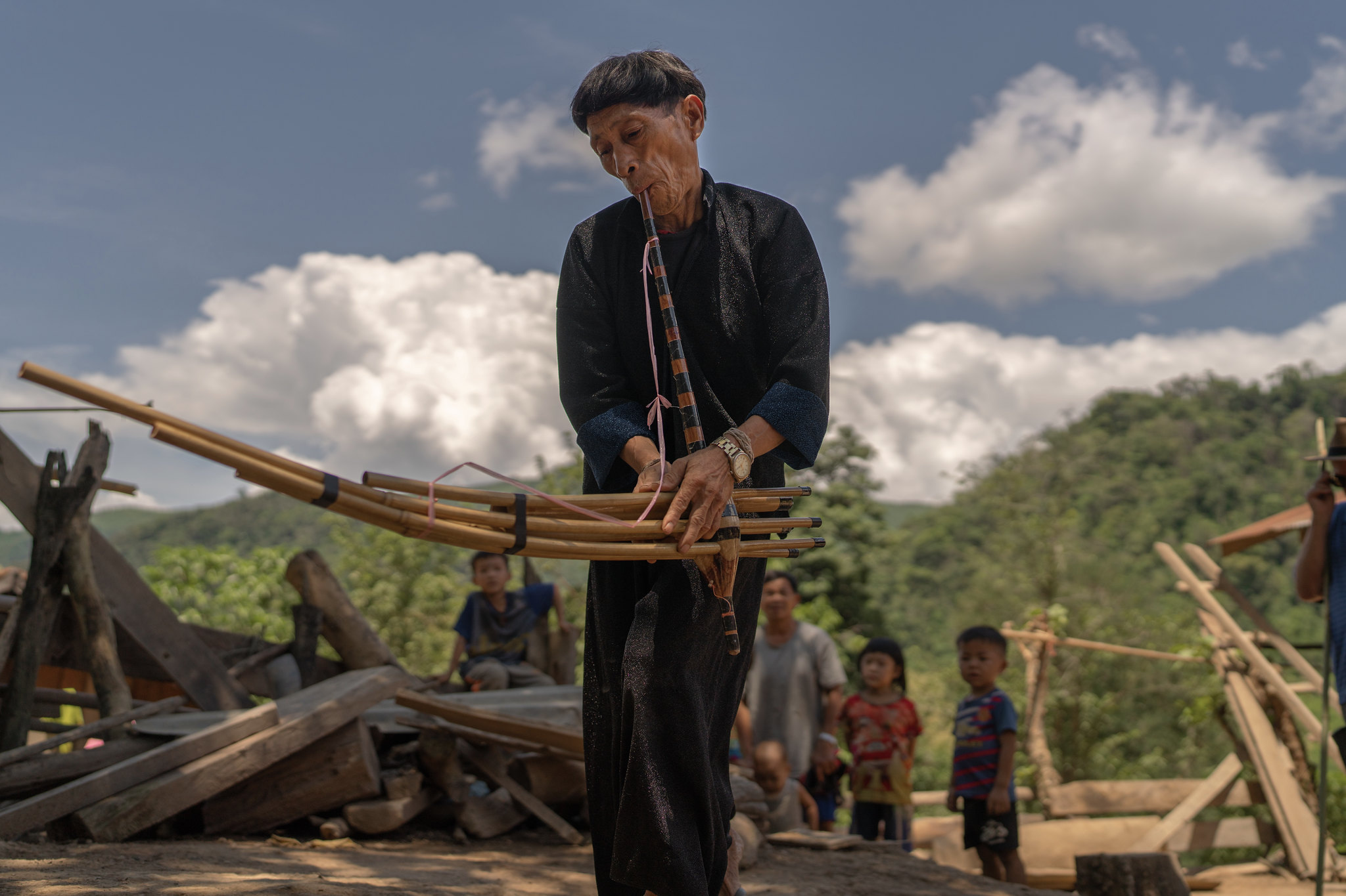 A musician playing bamboo pipes as children watch