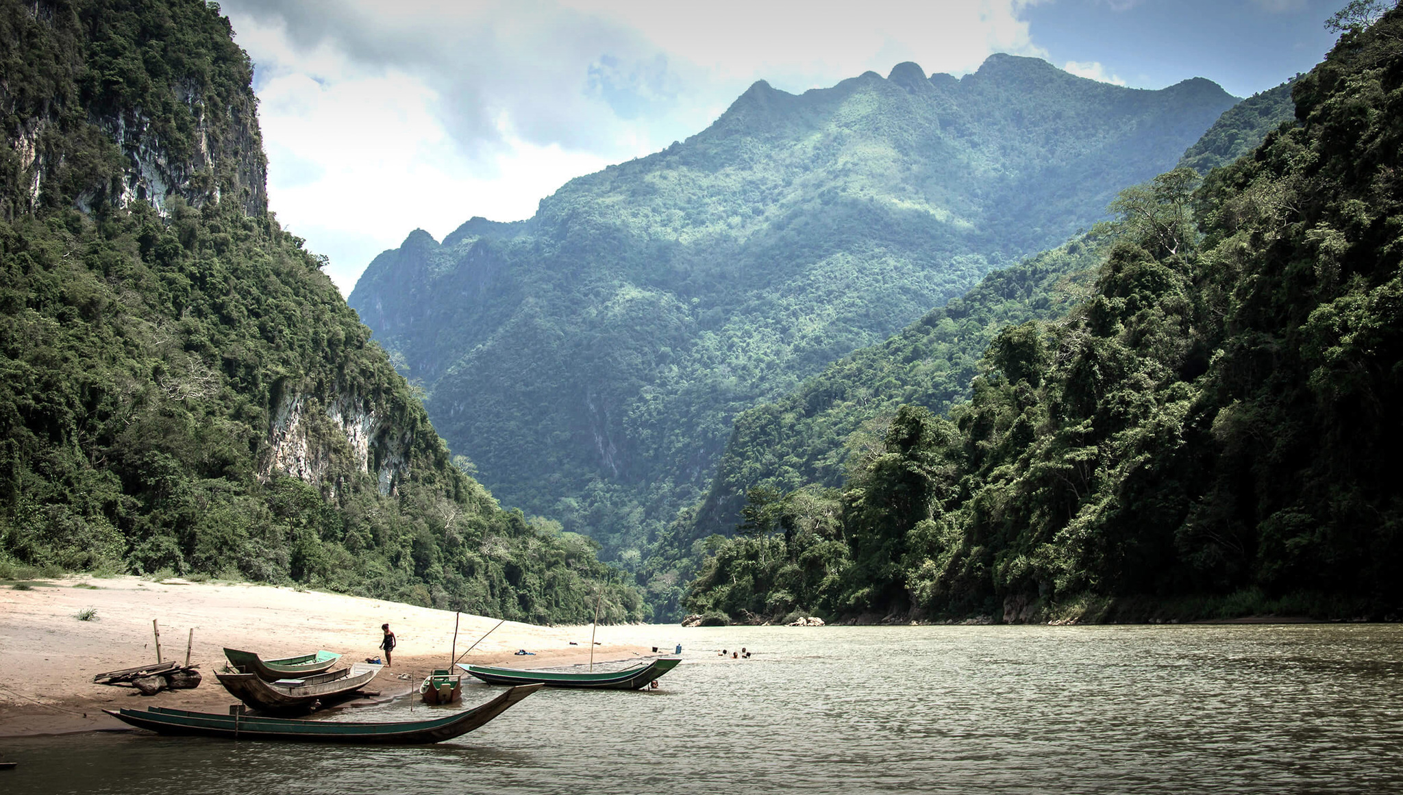 Longtail boats on a beach below forested limestone