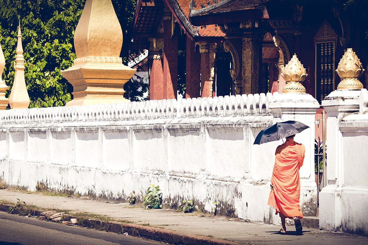 A monk with an umbrella beside a temple wall in Luang Prabang