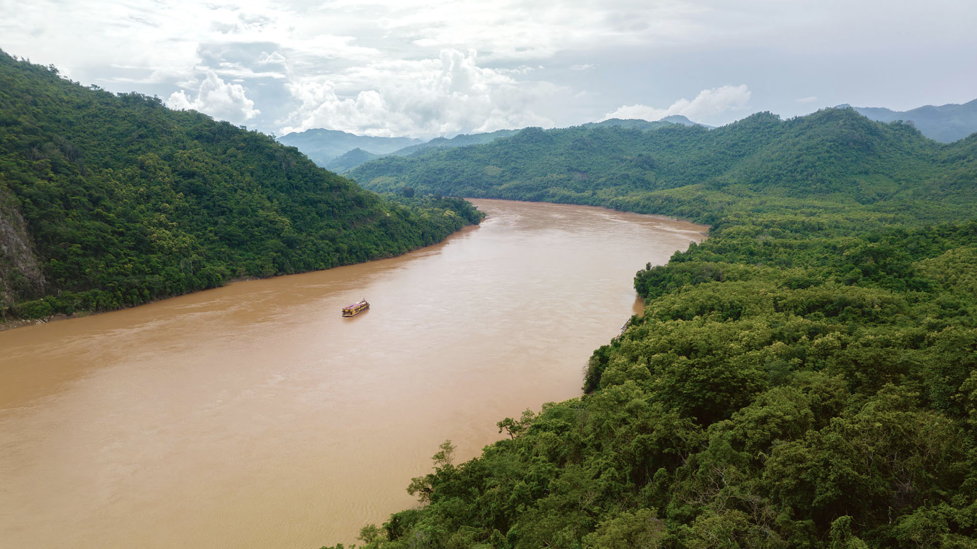 The Mekong between forested hills, a boat far below