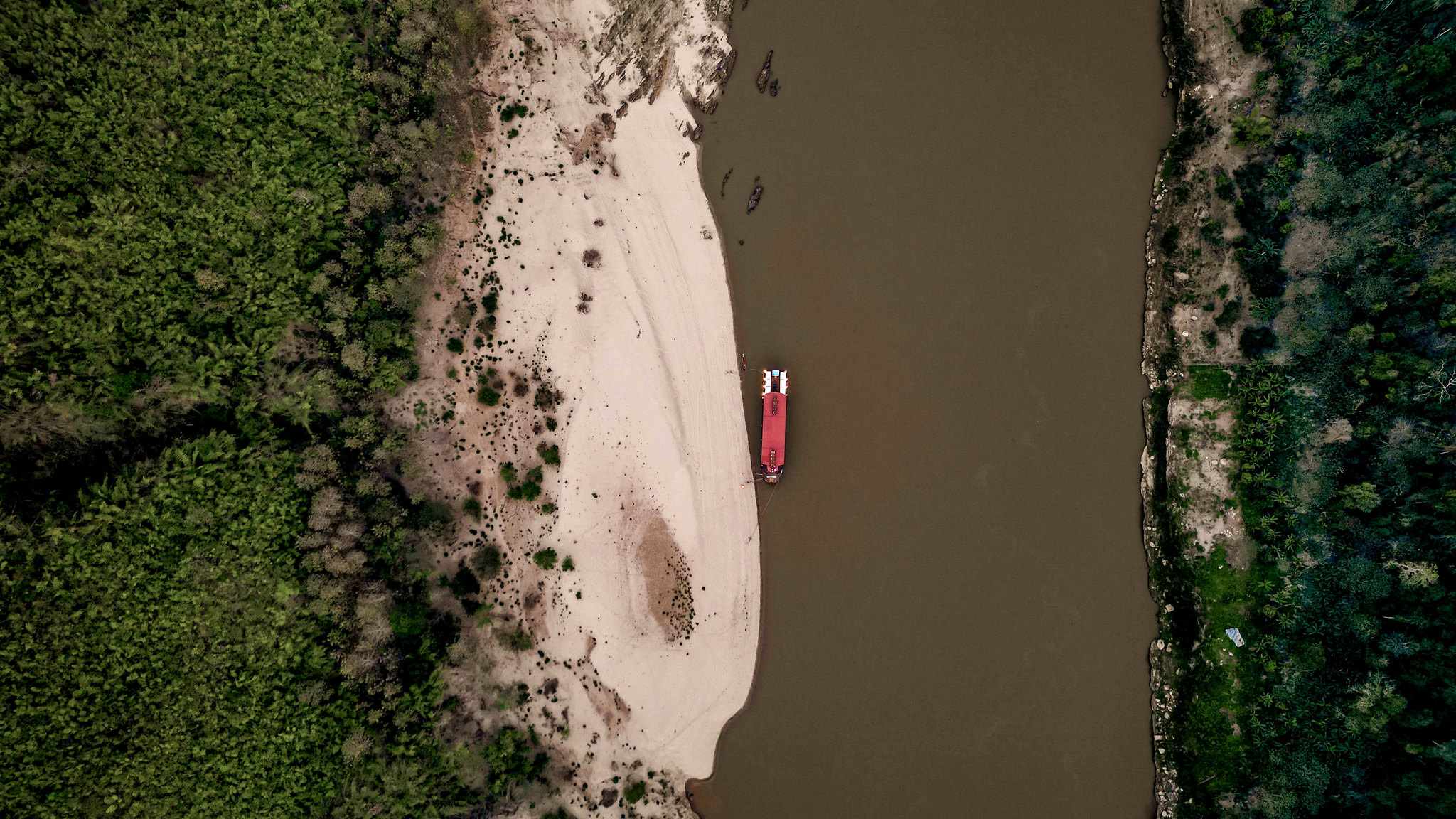 A red longtail moored at a white sandbar, from directly above