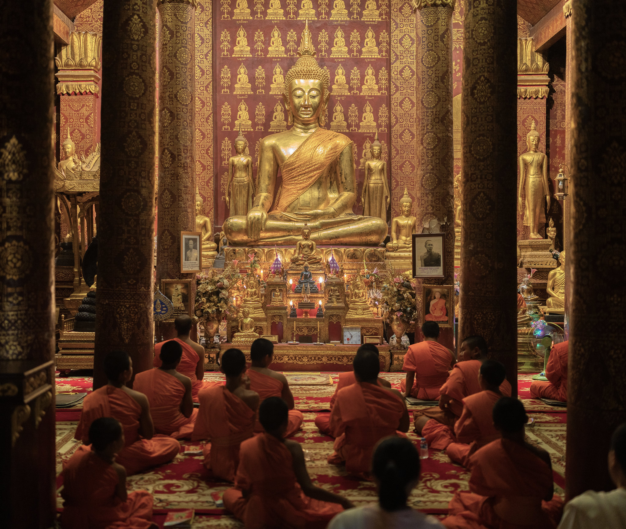 Monks chanting before a golden Buddha