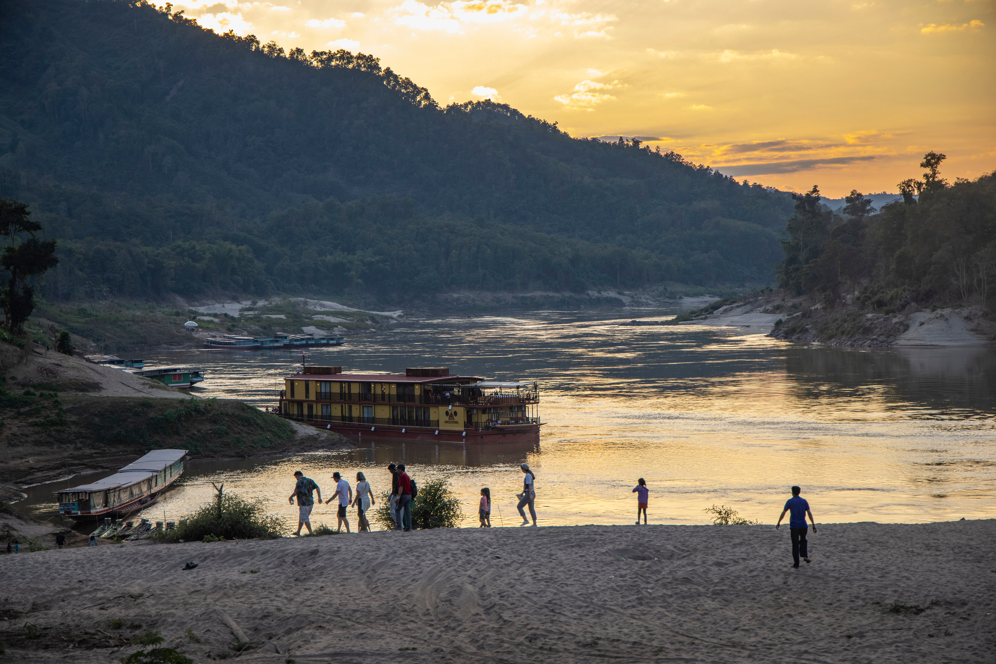 Guests on a sandbank at sunset, with the ship moored behind
