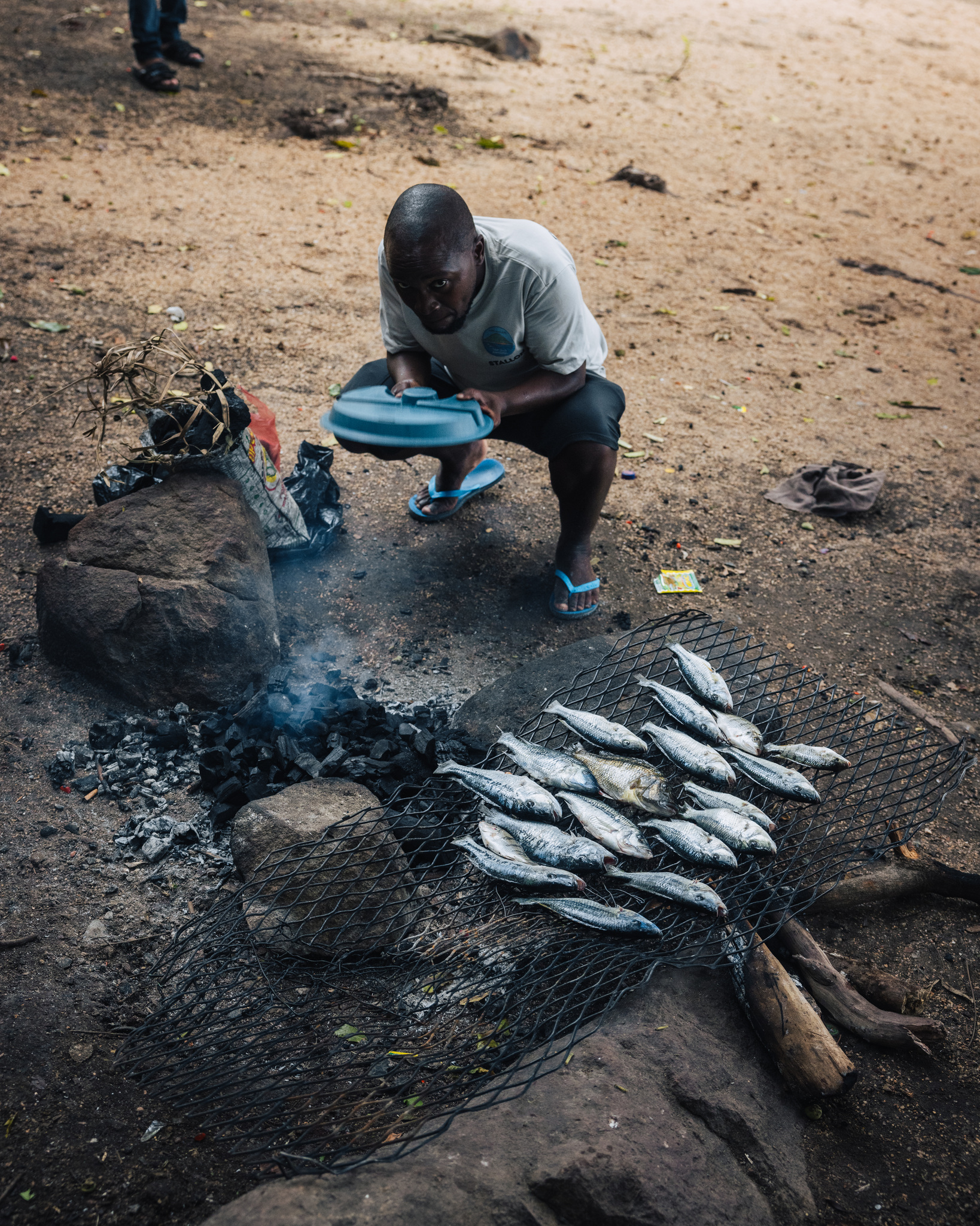 Fish grilling over charcoal on the shore