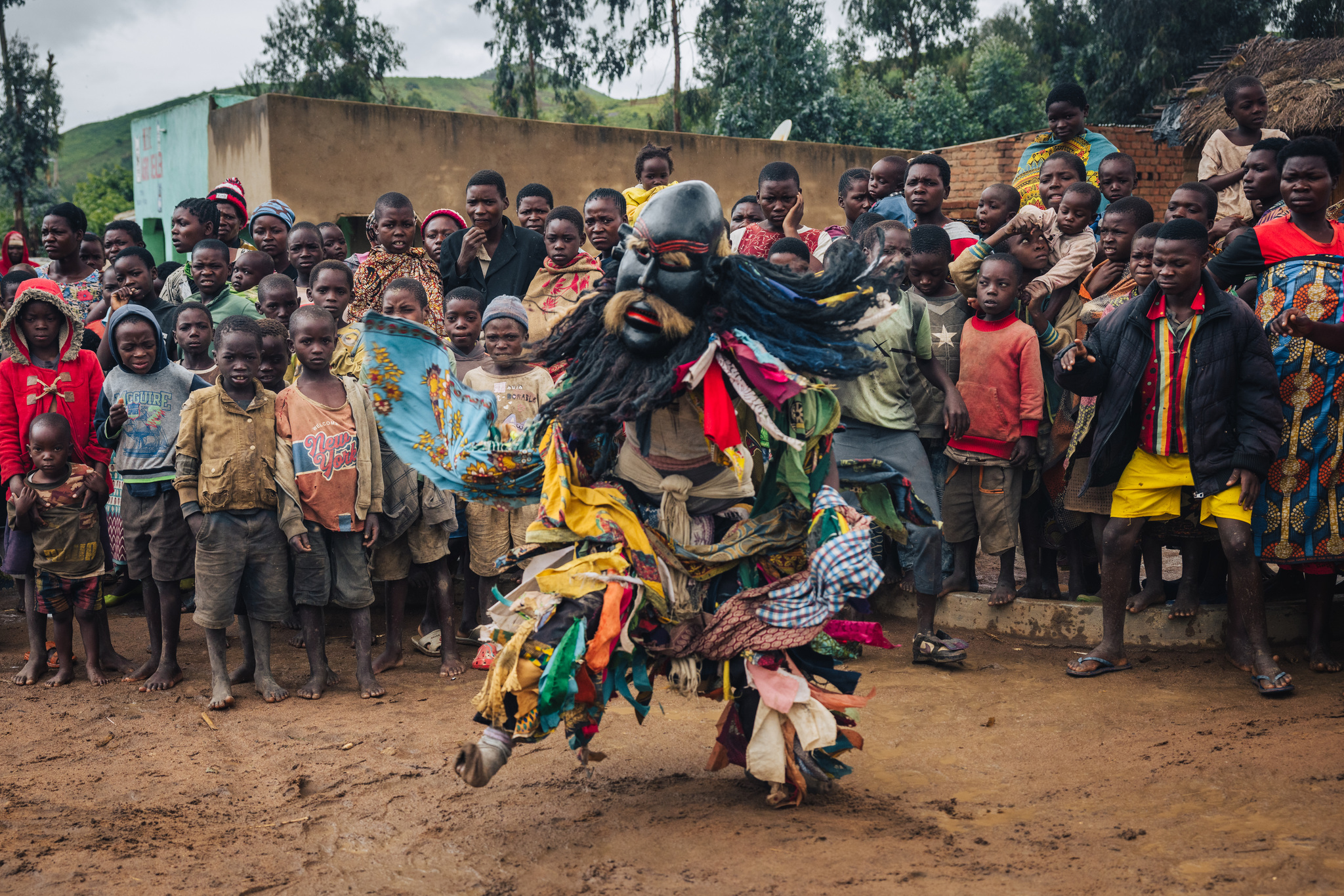 A bearded masked dancer before a crowd of villagers