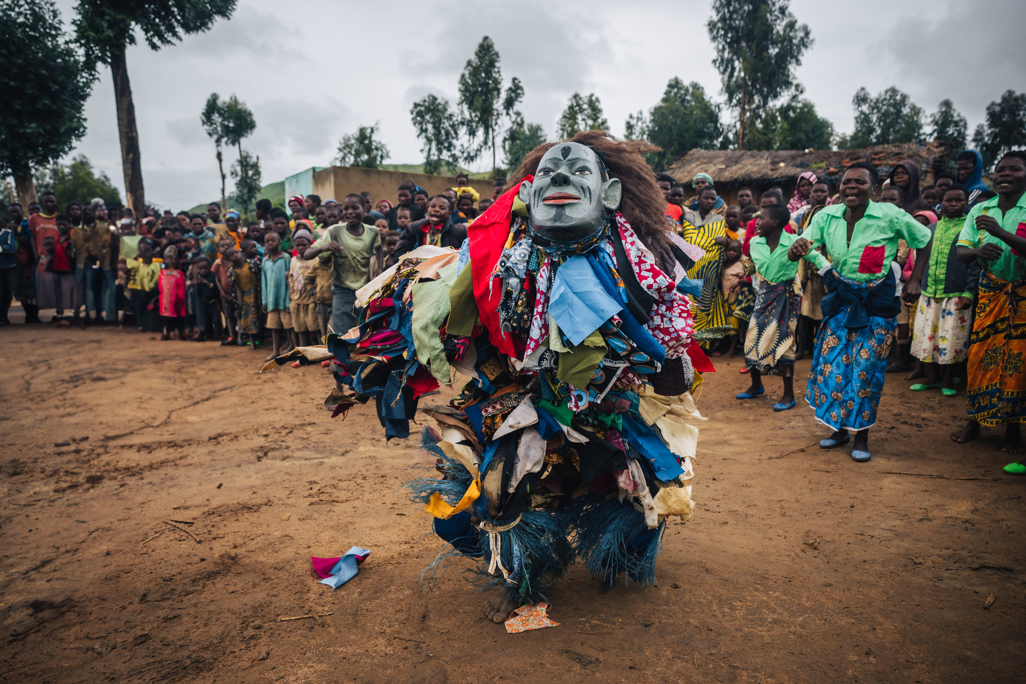 A Gule Wamkulu dancer in a pale mask, the village women behind