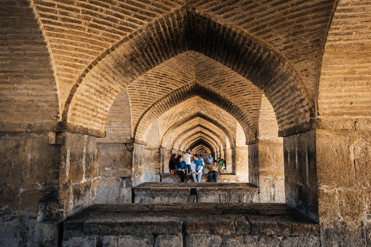 Families sitting in the arches beneath the Khaju Bridge over the Zayandeh Rud, Isfahan