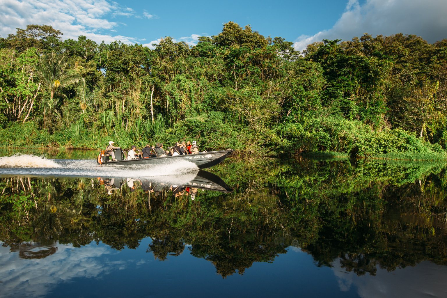A skiff speeding past forest reflected in the river