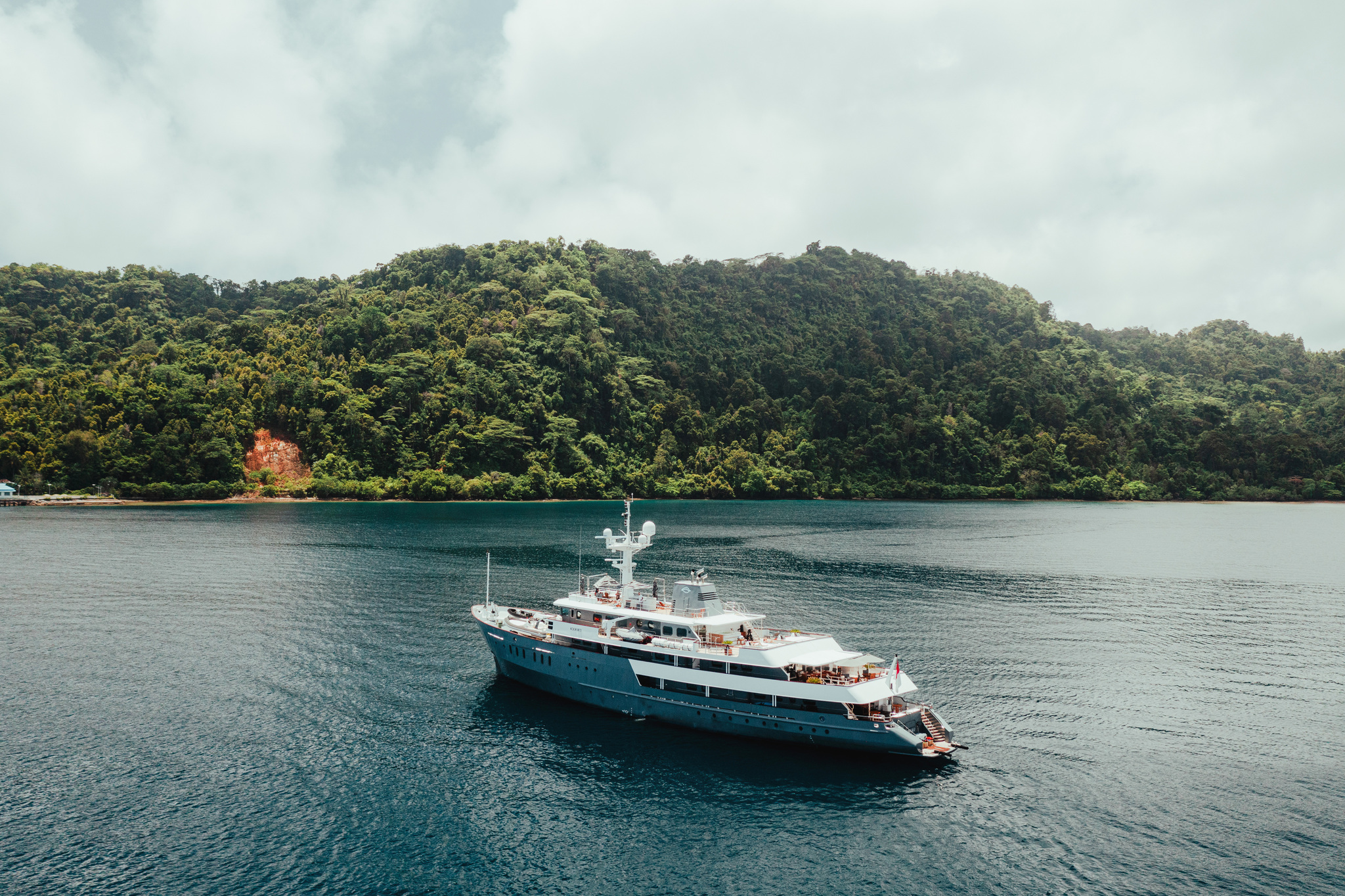 Aqua Blu at anchor in a calm bay below forested hills