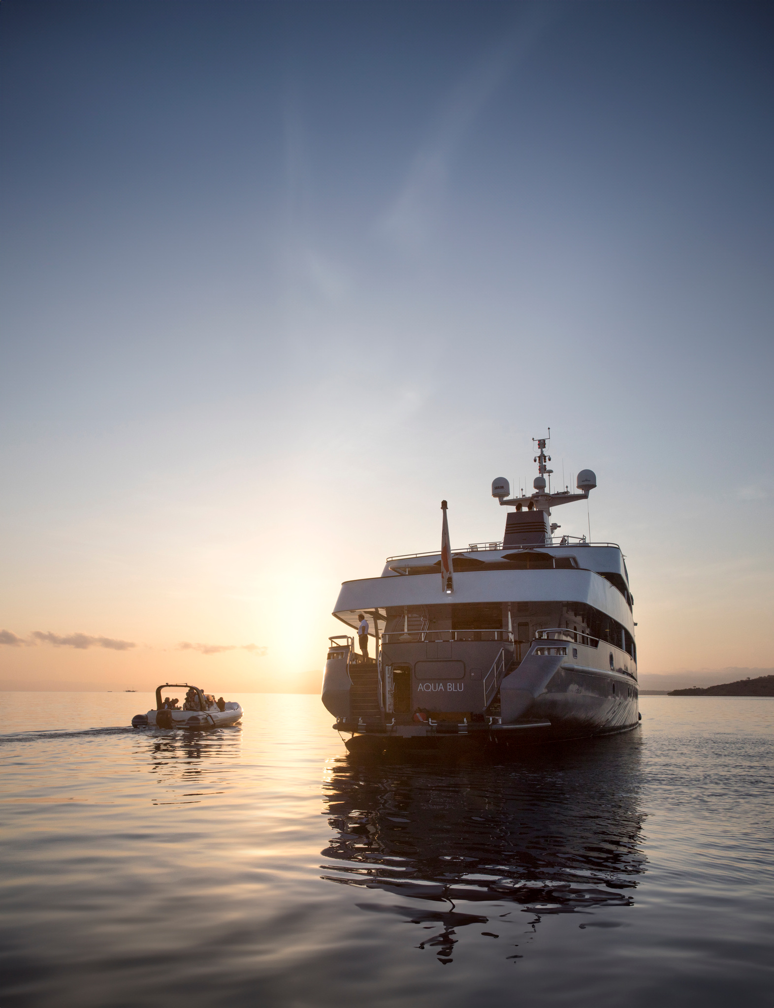 Aqua Blu at anchor at sunset, a tender crossing the calm water beside her