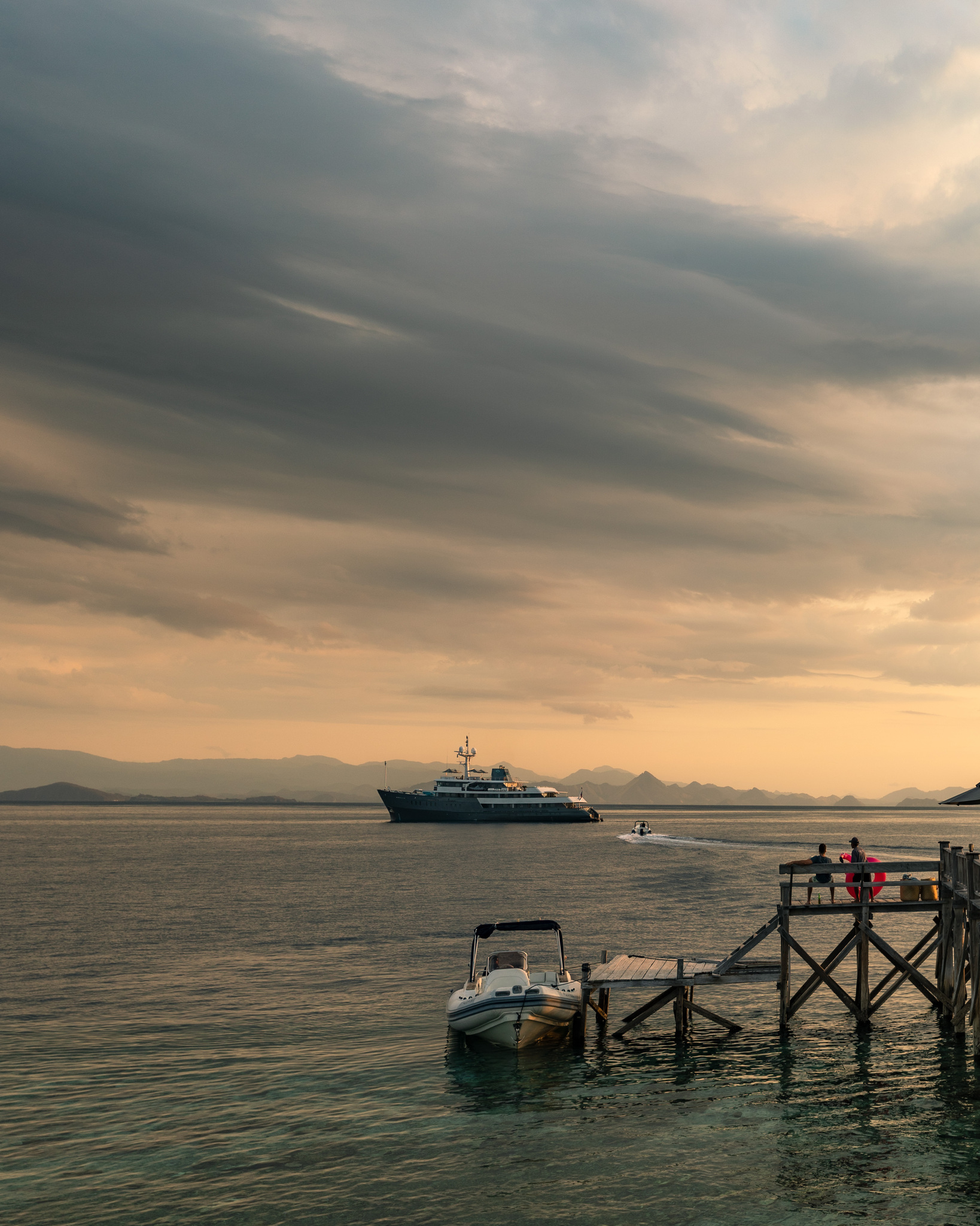 Aqua Blu offshore under an evening sky, seen past a wooden jetty and a moored boat