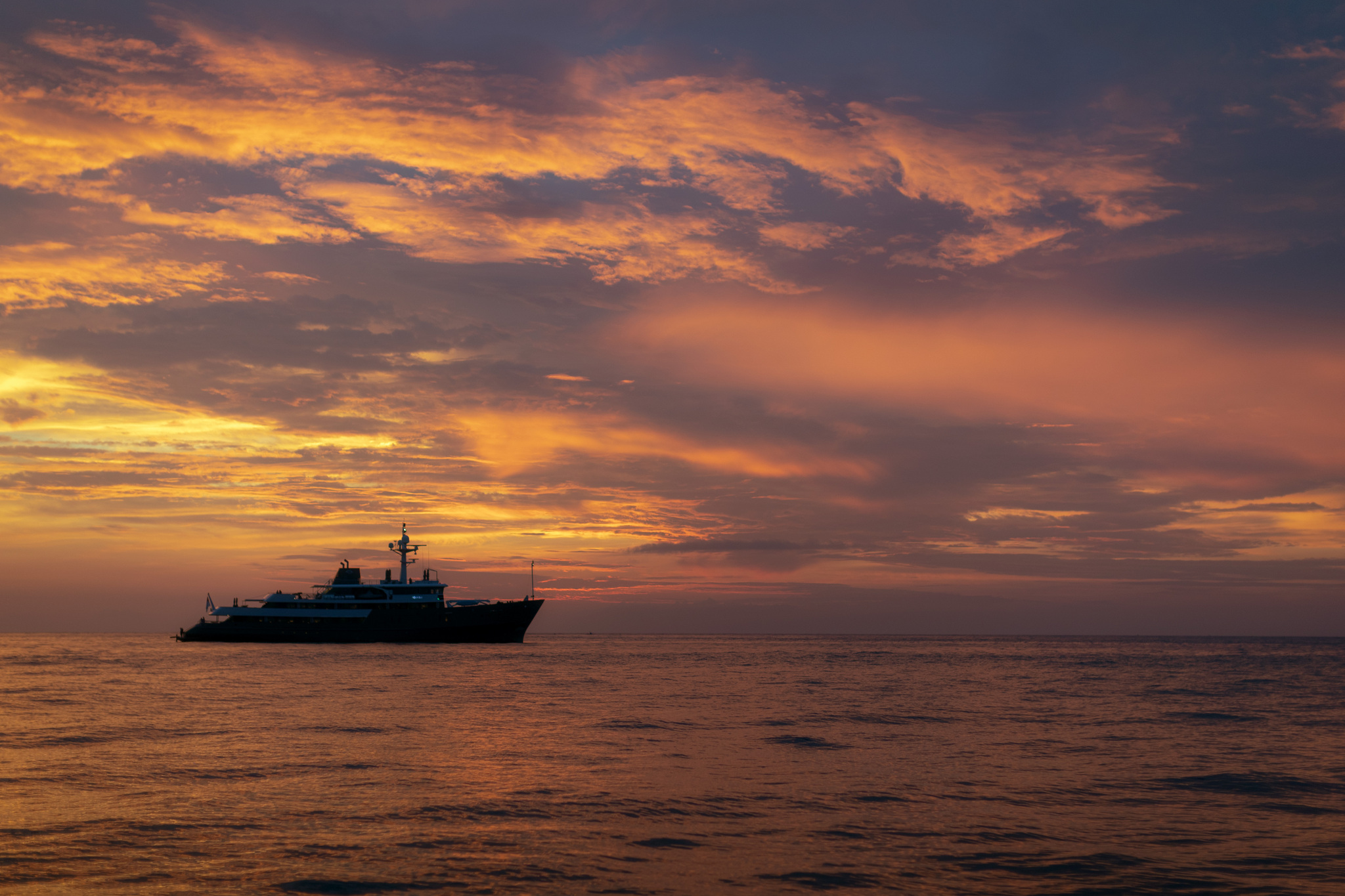 Aqua Blu in silhouette on the open sea under an orange sunset sky