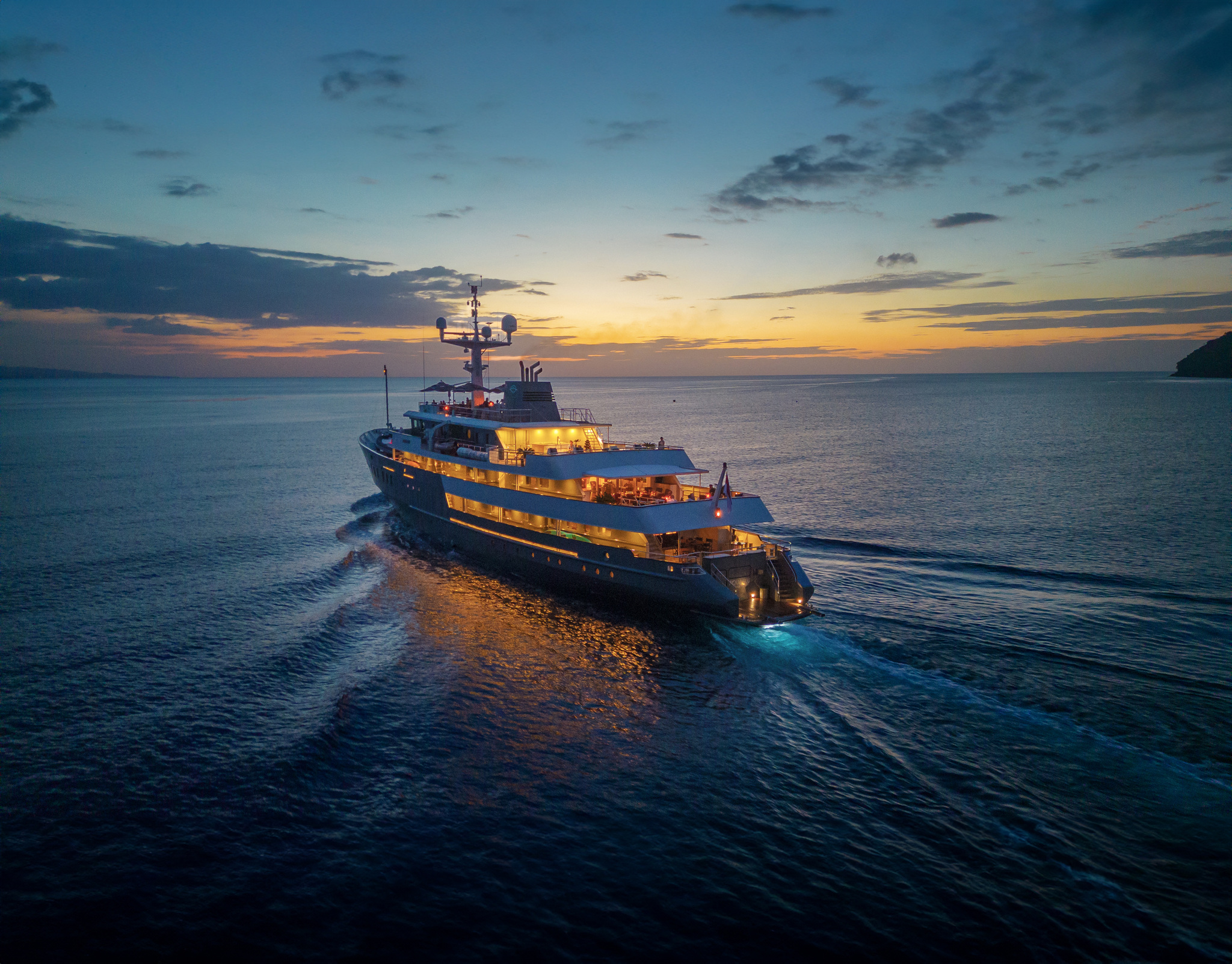 Aqua Blu under way at dusk, her decks lit and a pale wake behind