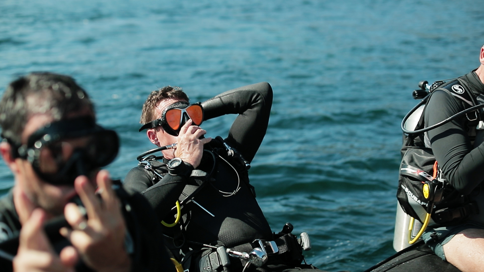 Divers in wetsuits fitting their masks on the side of a tender