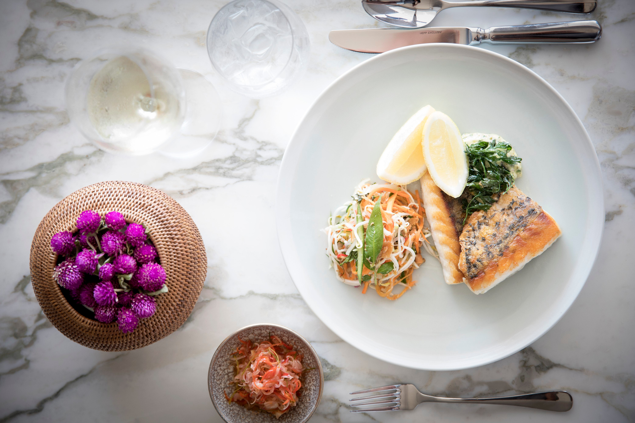 Grilled fish with lemon, greens and a shredded salad, beside a small bowl of red relish