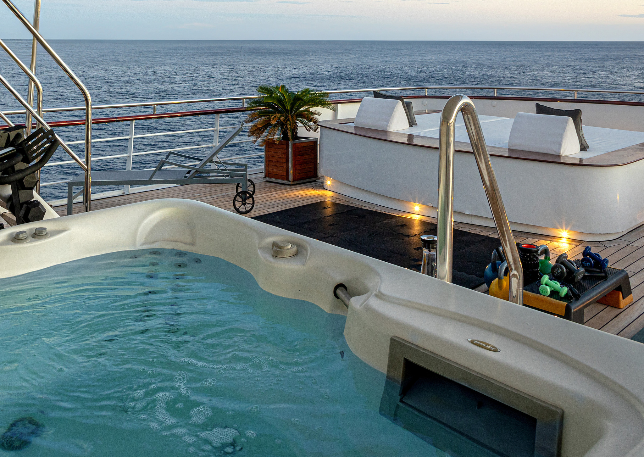 The jacuzzi on the bridge deck at dusk, with weights beside it and the sea beyond