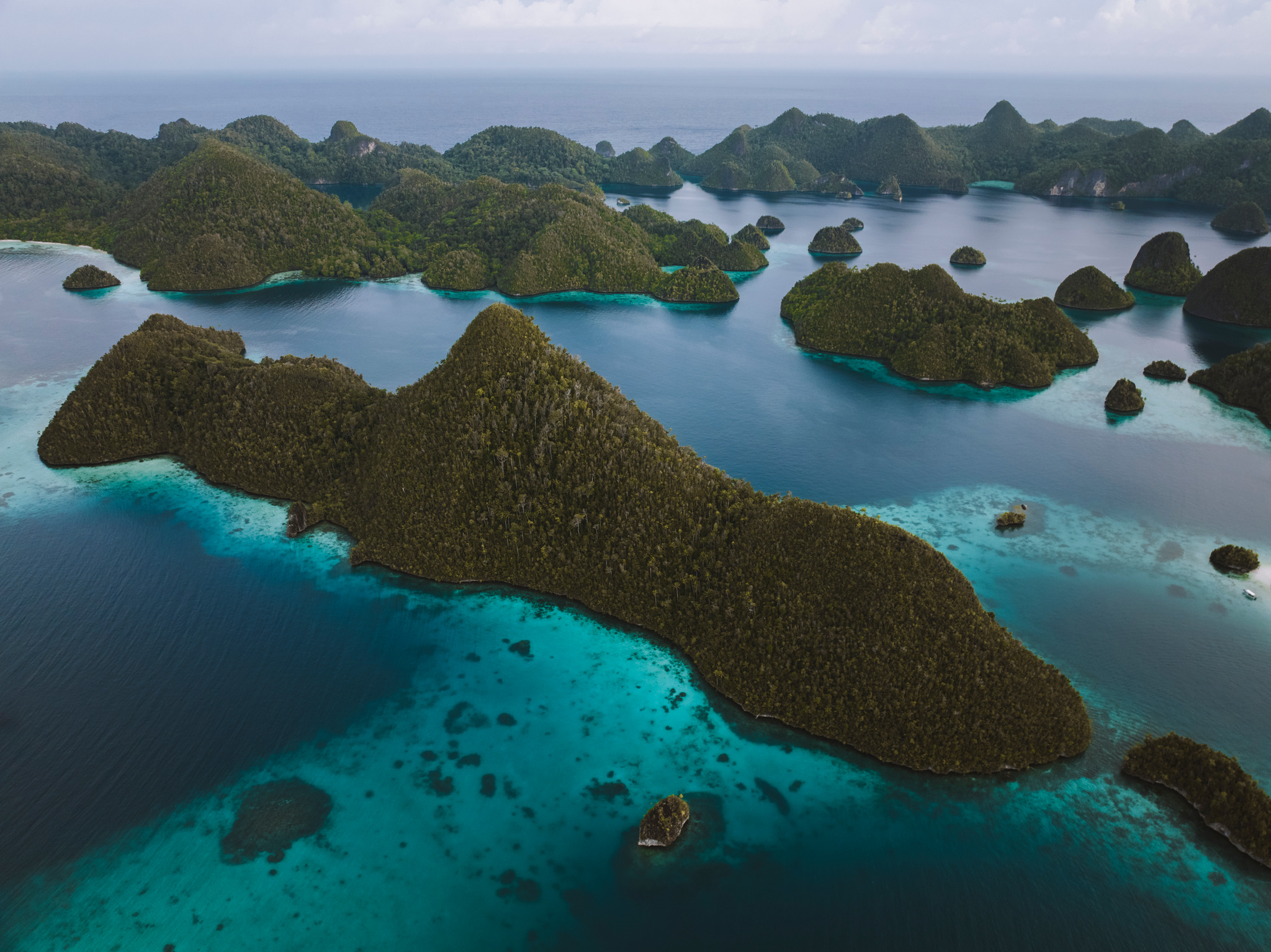 Dozens of steep forested islands scattered across calm water, with reefs between them